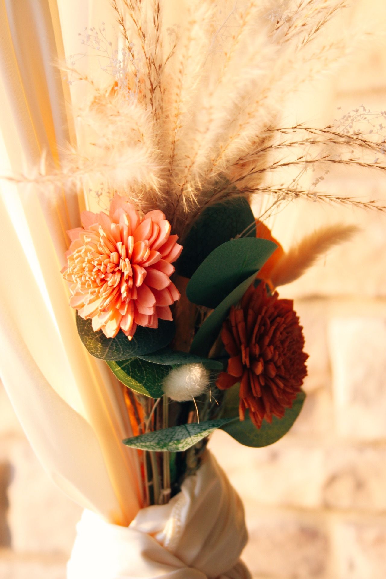 Autumn bouquet with peach dahlias, dried pampas grass, eucalyptus leaves, and silver brunia in warm golden light.
