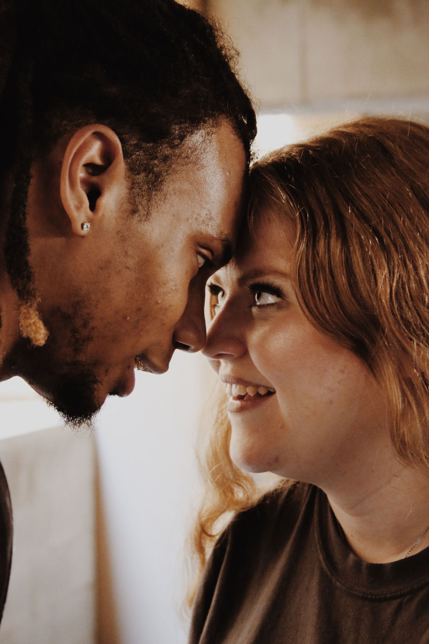 Romantic interracial couple sharing an intimate moment, touching foreheads and smiling tenderly at each other.