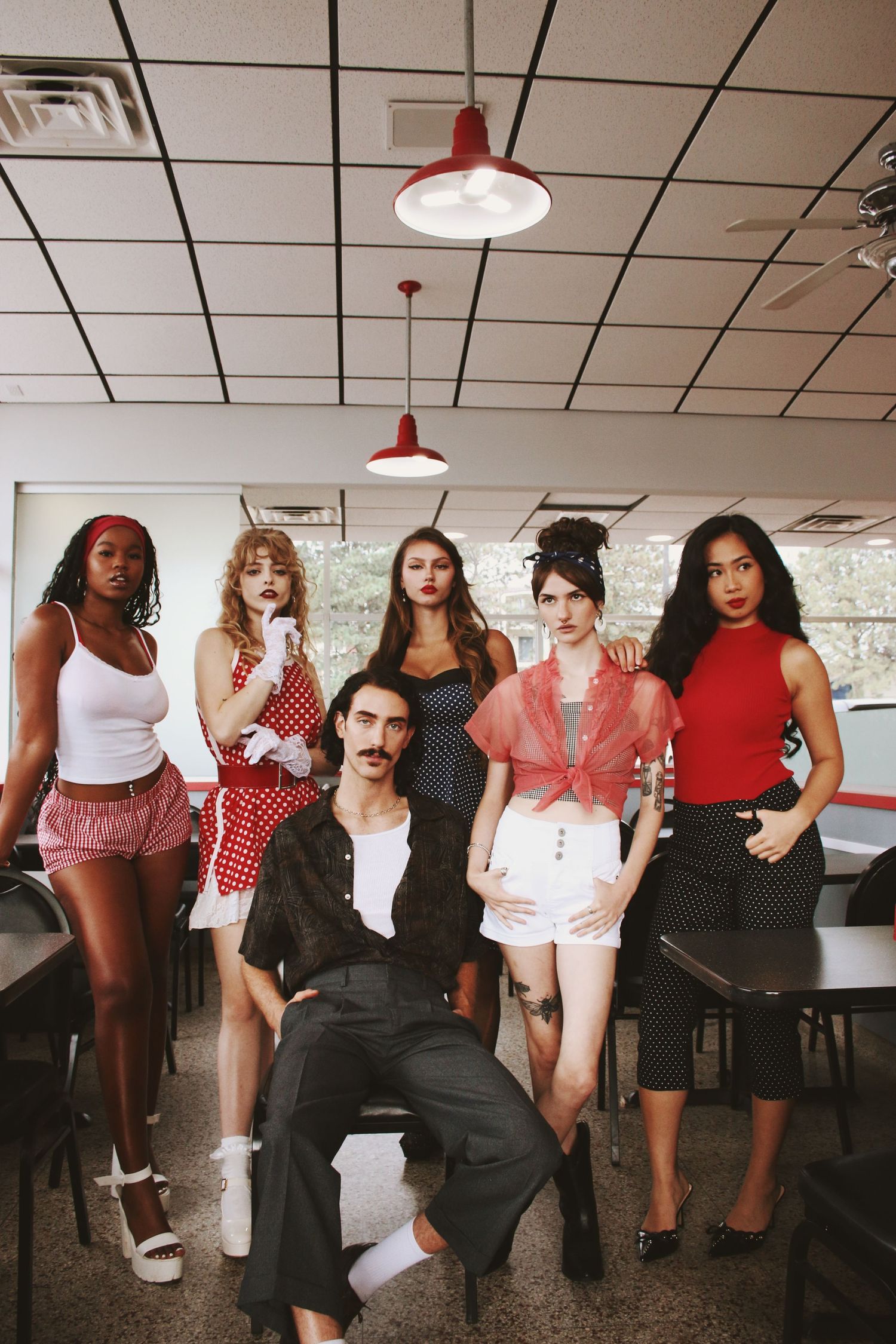 Six stylish models pose in a retro diner setting, wearing vintage-inspired outfits in red, white, and black.