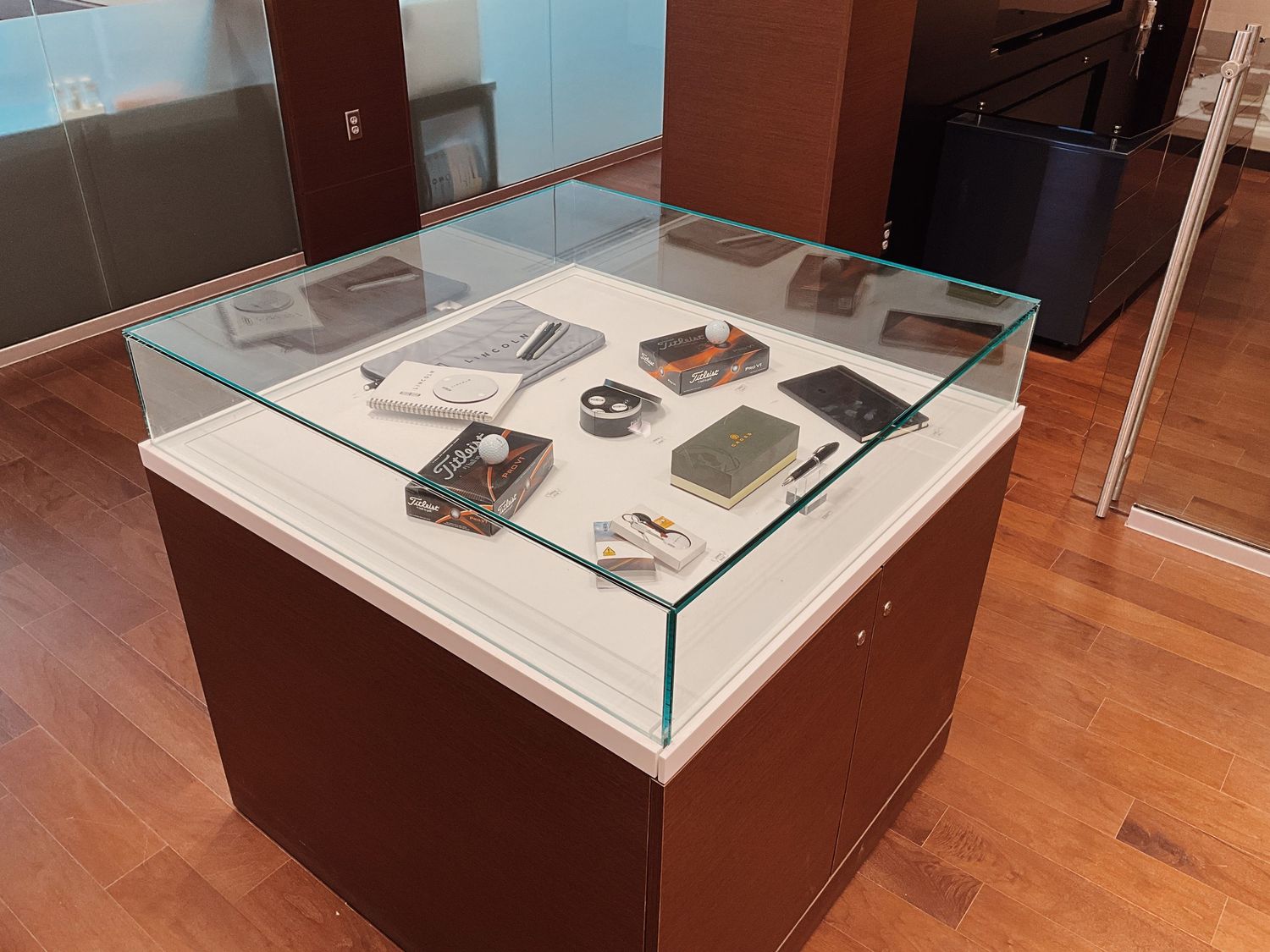 Museum display case with glass top showcasing vintage electronic devices and small artifacts on white pedestal.