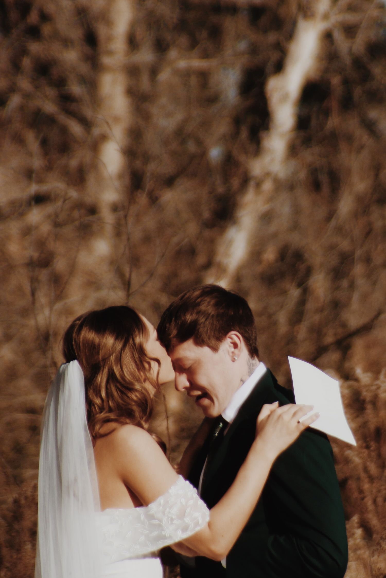 Bride and groom sharing an intimate moment, touching foreheads and smiling, with a blurred autumn background.