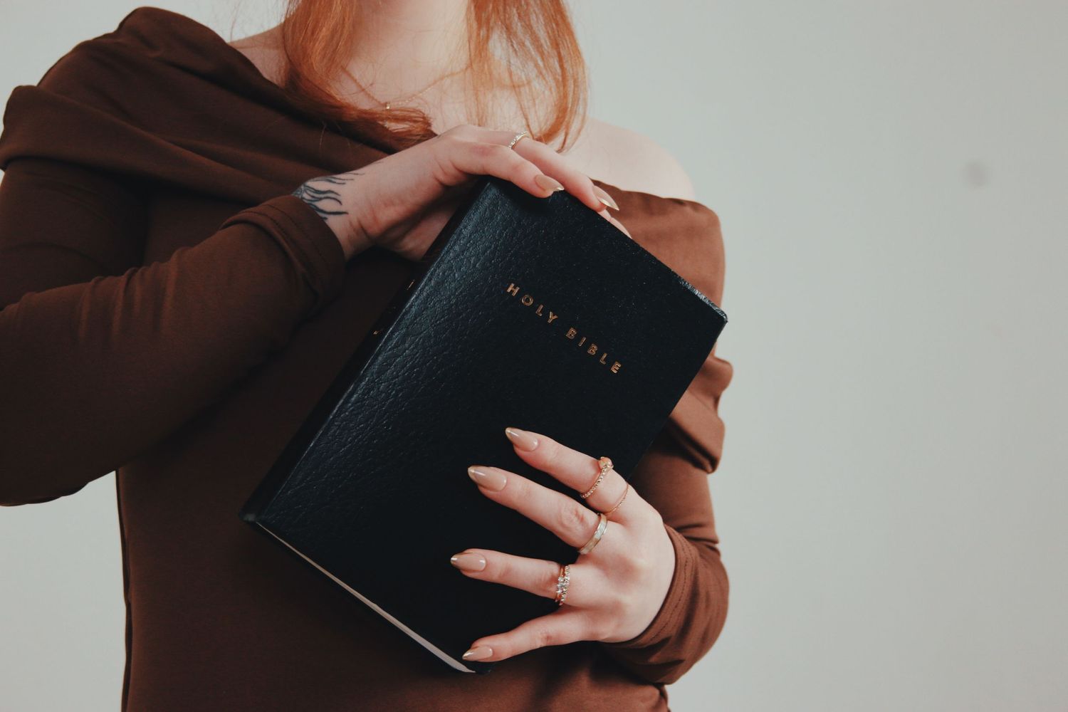 Woman in brown off-shoulder top holding a black Holy Bible close to her chest.