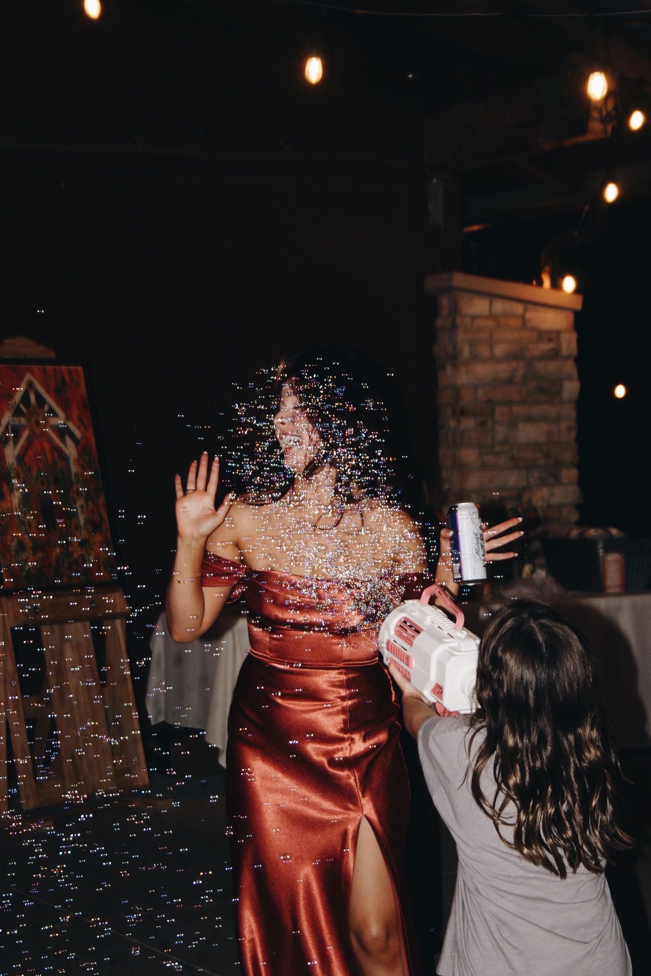 Woman in red satin dress reacts to confetti cannon at festive indoor celebration event.