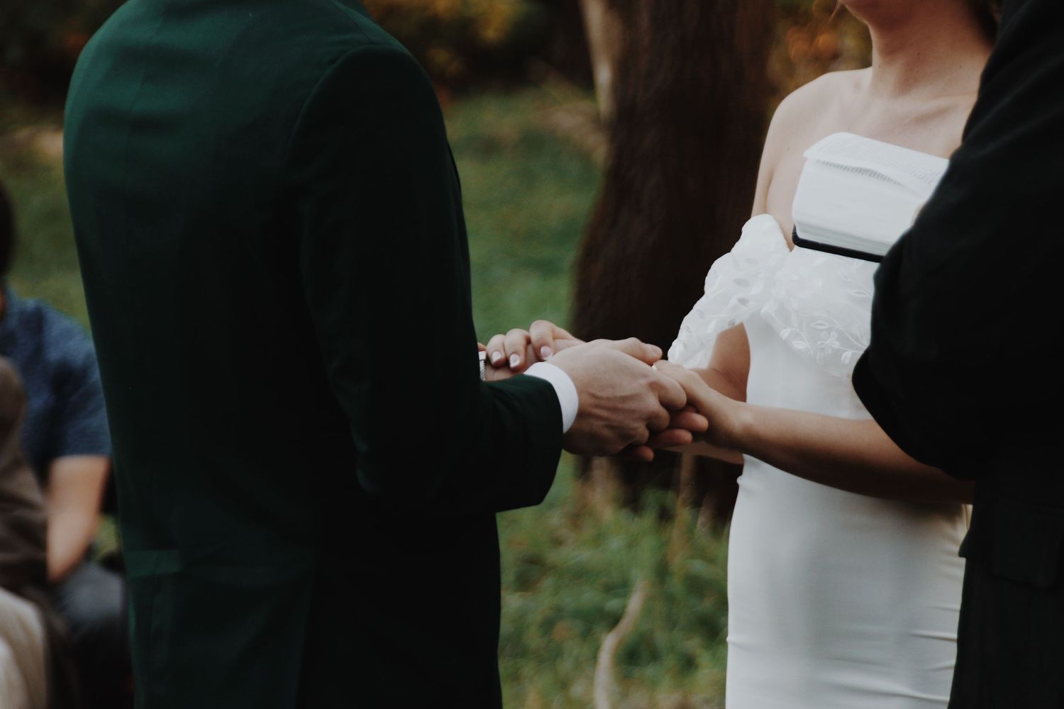 Bride and groom holding hands during outdoor wedding ceremony, bride in white strapless gown.