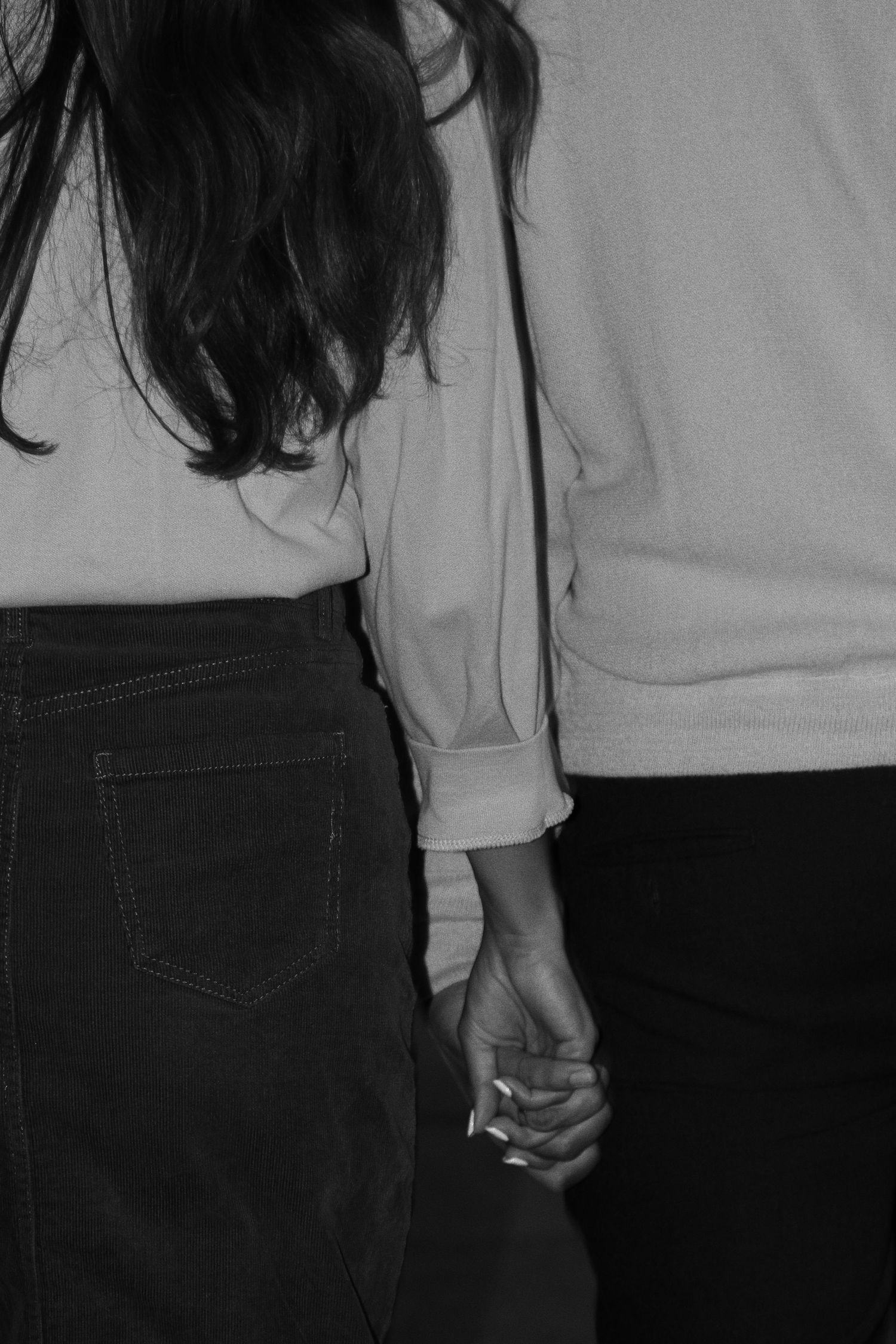Black and white photo of two people holding hands, one wearing a white shirt and jeans, the other in a light sweater.
