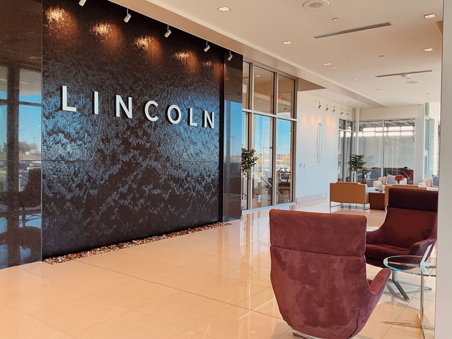 Modern Lincoln dealership lobby with a textured feature wall, sleek flooring, and plush burgundy seating chairs.