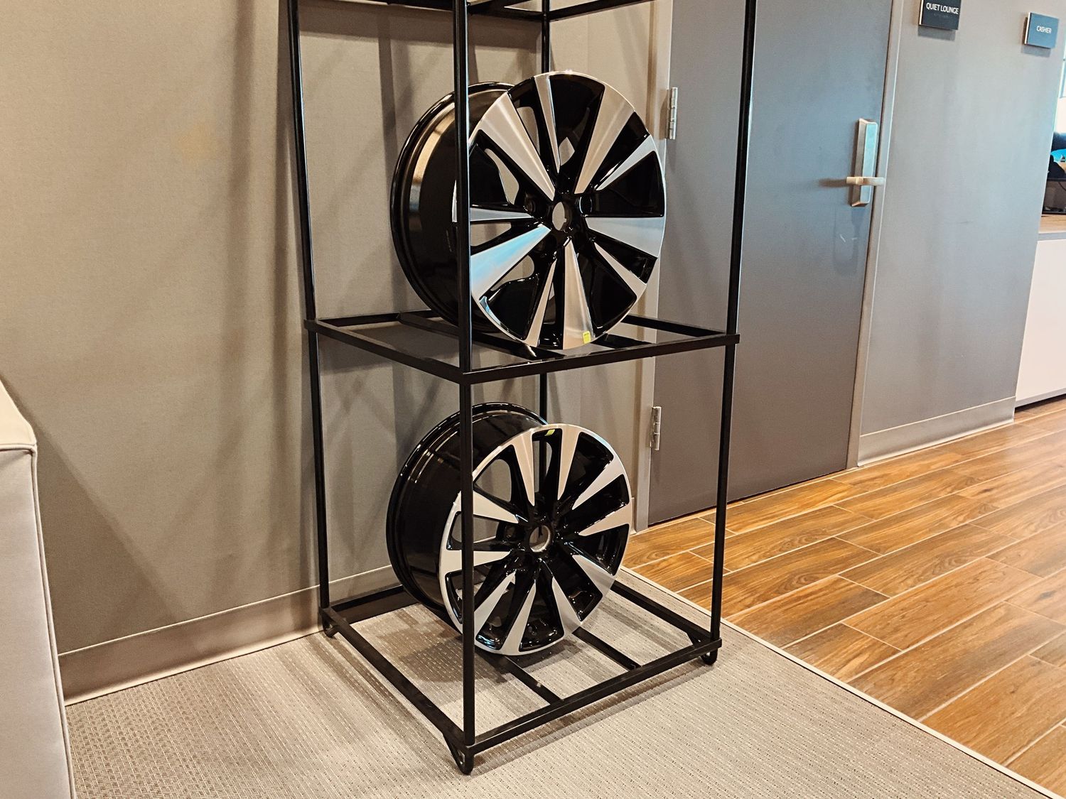 Two black and silver alloy wheels displayed on a metal rack shelf unit indoors.