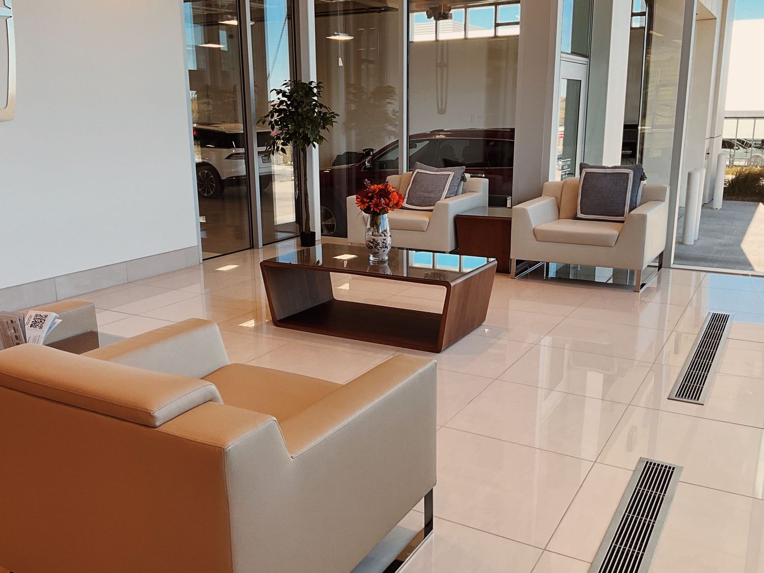 Luxury car dealership showroom lounge with modern white and tan leather chairs and glass coffee table.