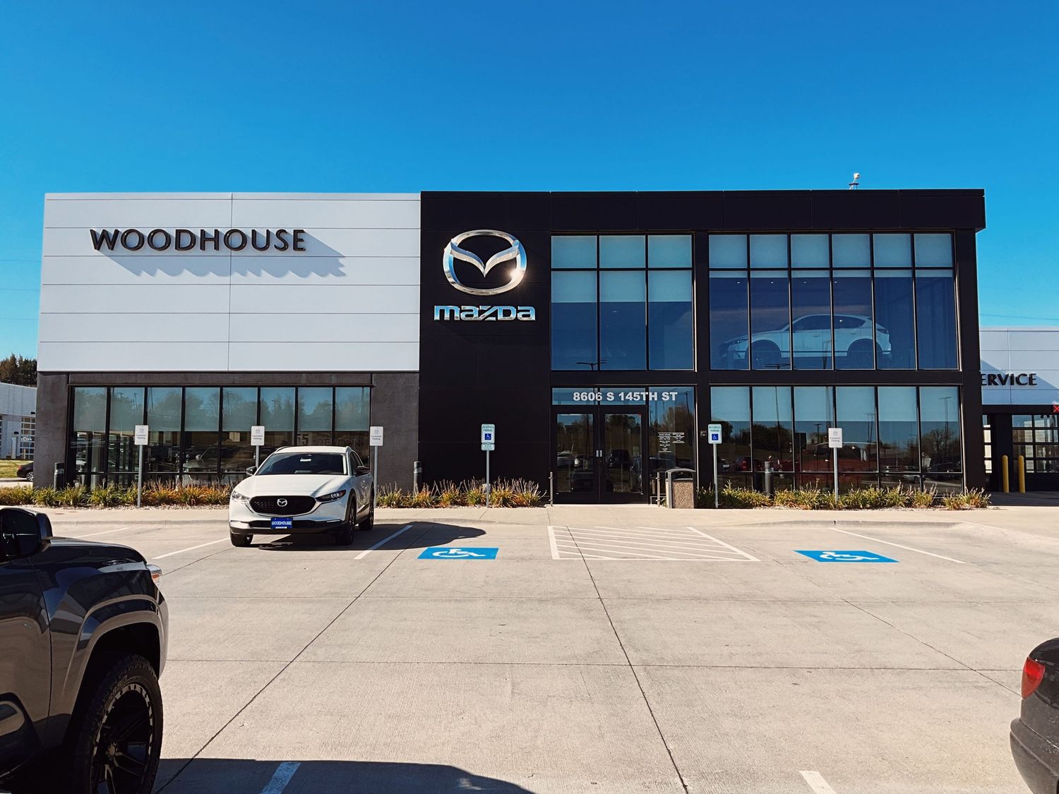 Woodhouse Mazda dealership exterior featuring modern black and white facade with large windows and parking lot.