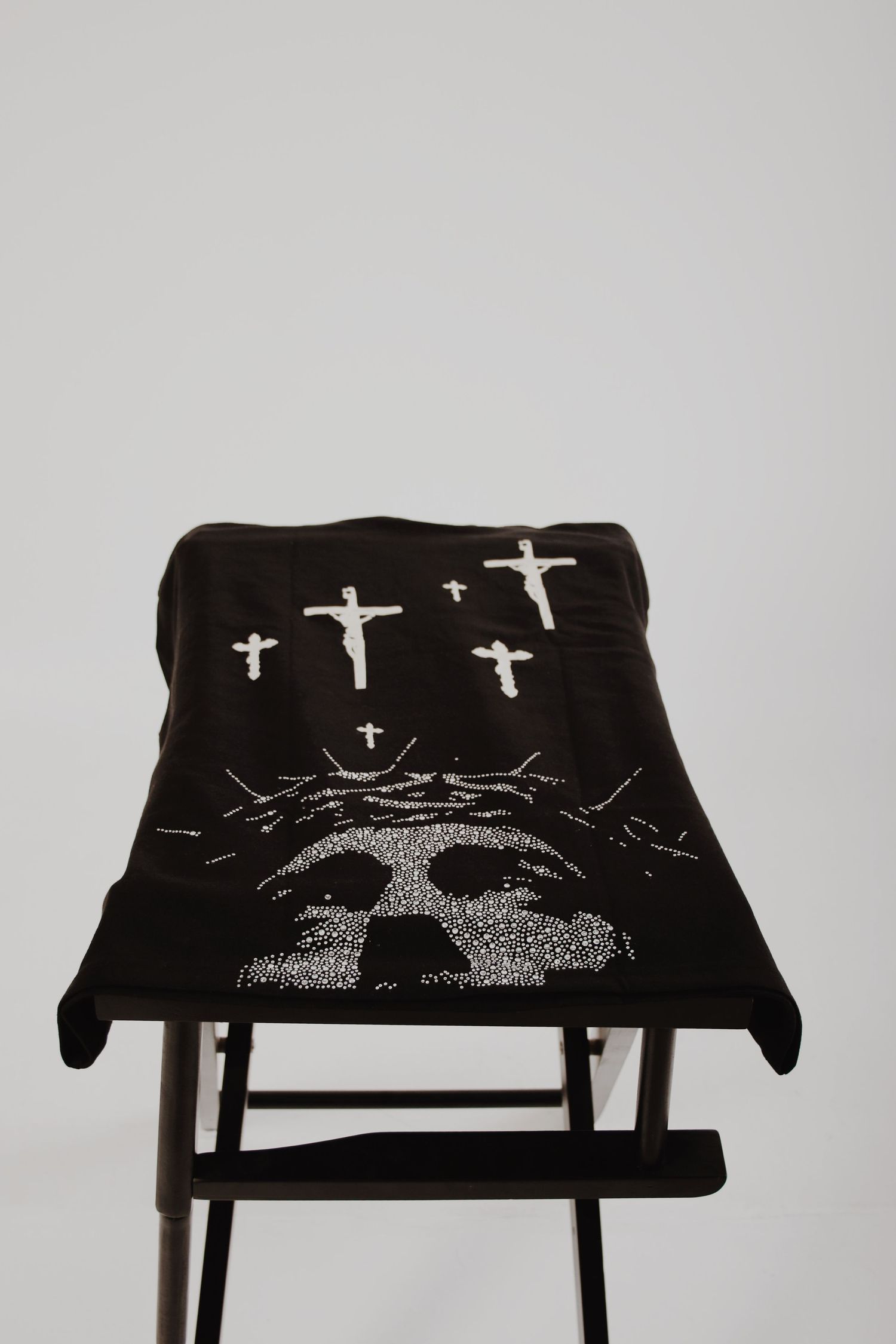 Black knit blanket with skull and crosses design draped over a folding chair against white background.