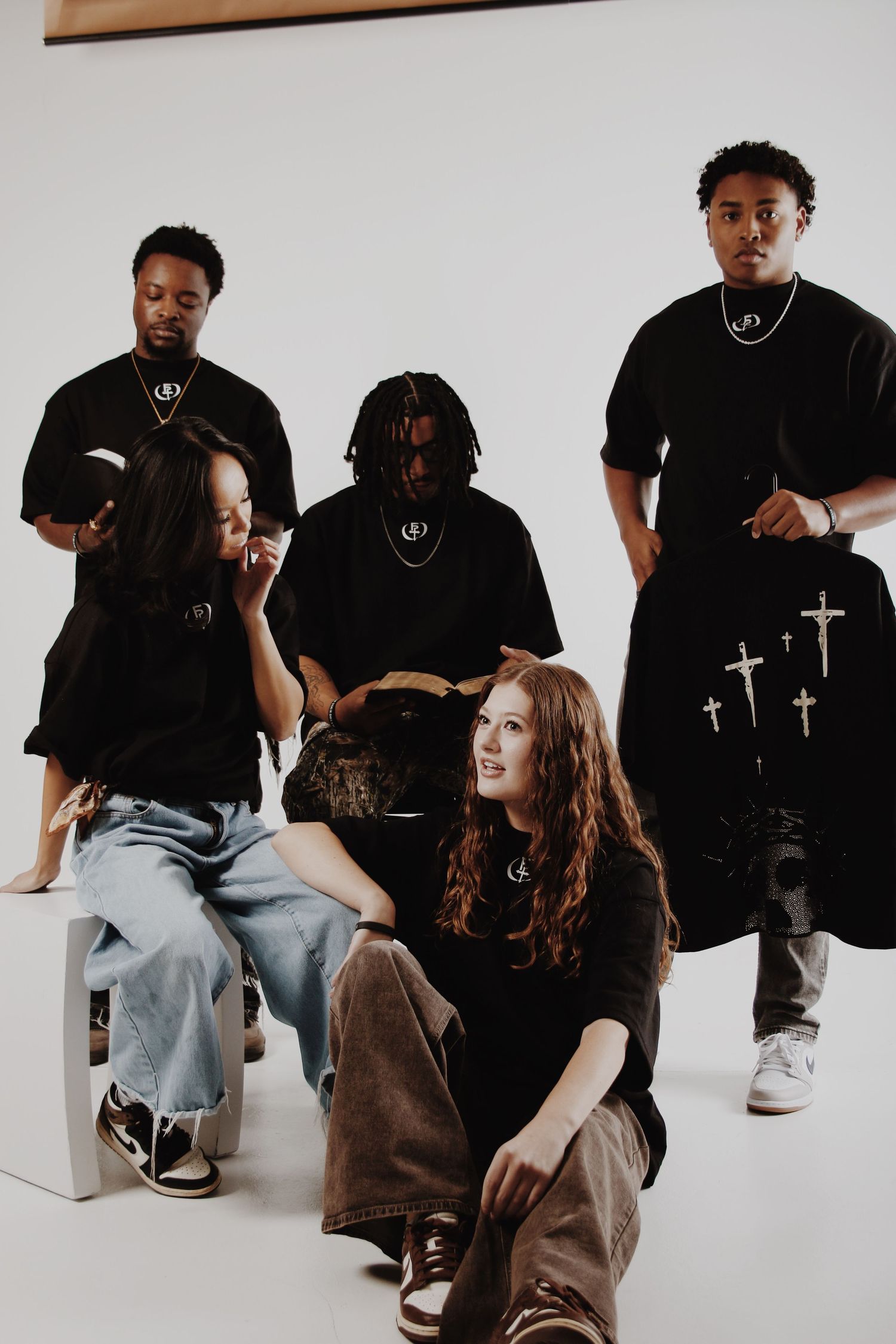 Group of five young adults in matching black outfits posing together in a bright white studio setting.