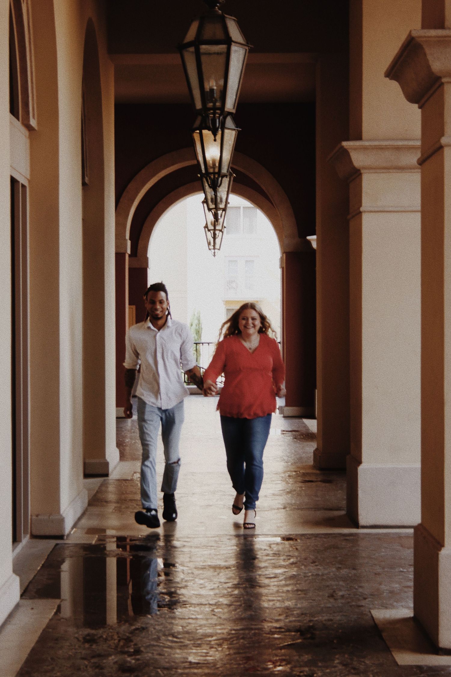 Couple holding hands and walking through an elegant arched colonnade corridor with vintage lanterns.