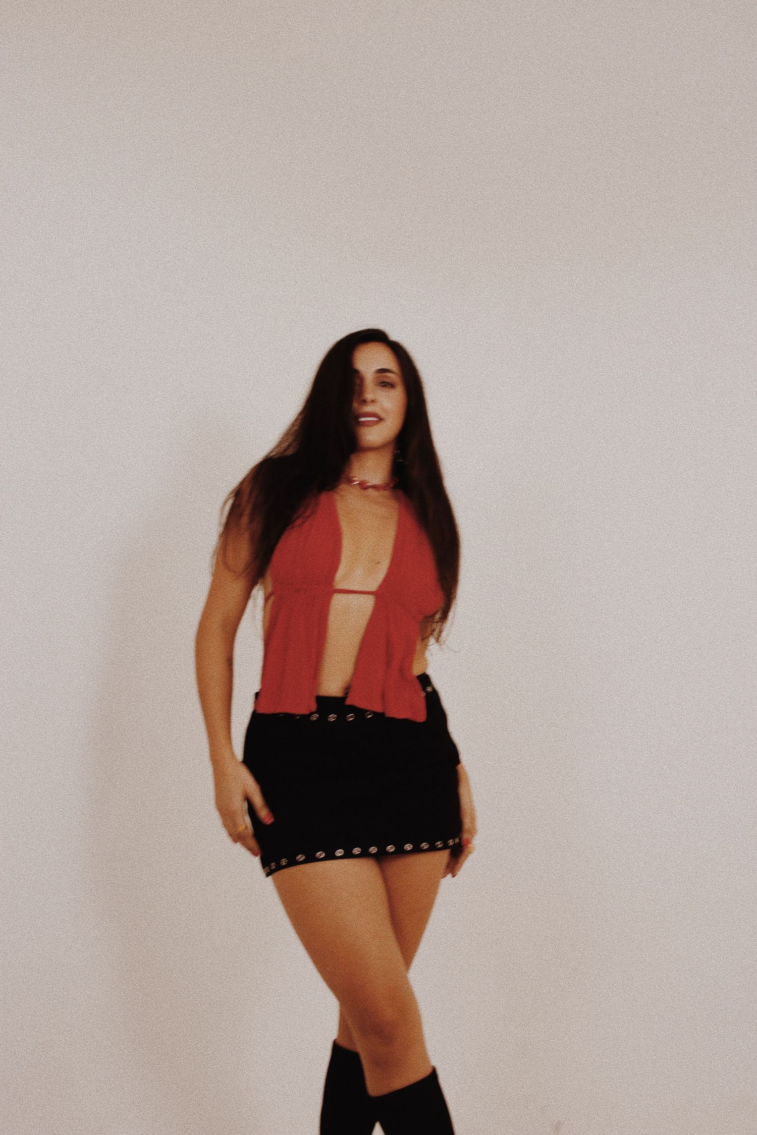 Young woman in red halter top, black mini skirt, and knee-high boots posing against white background.
