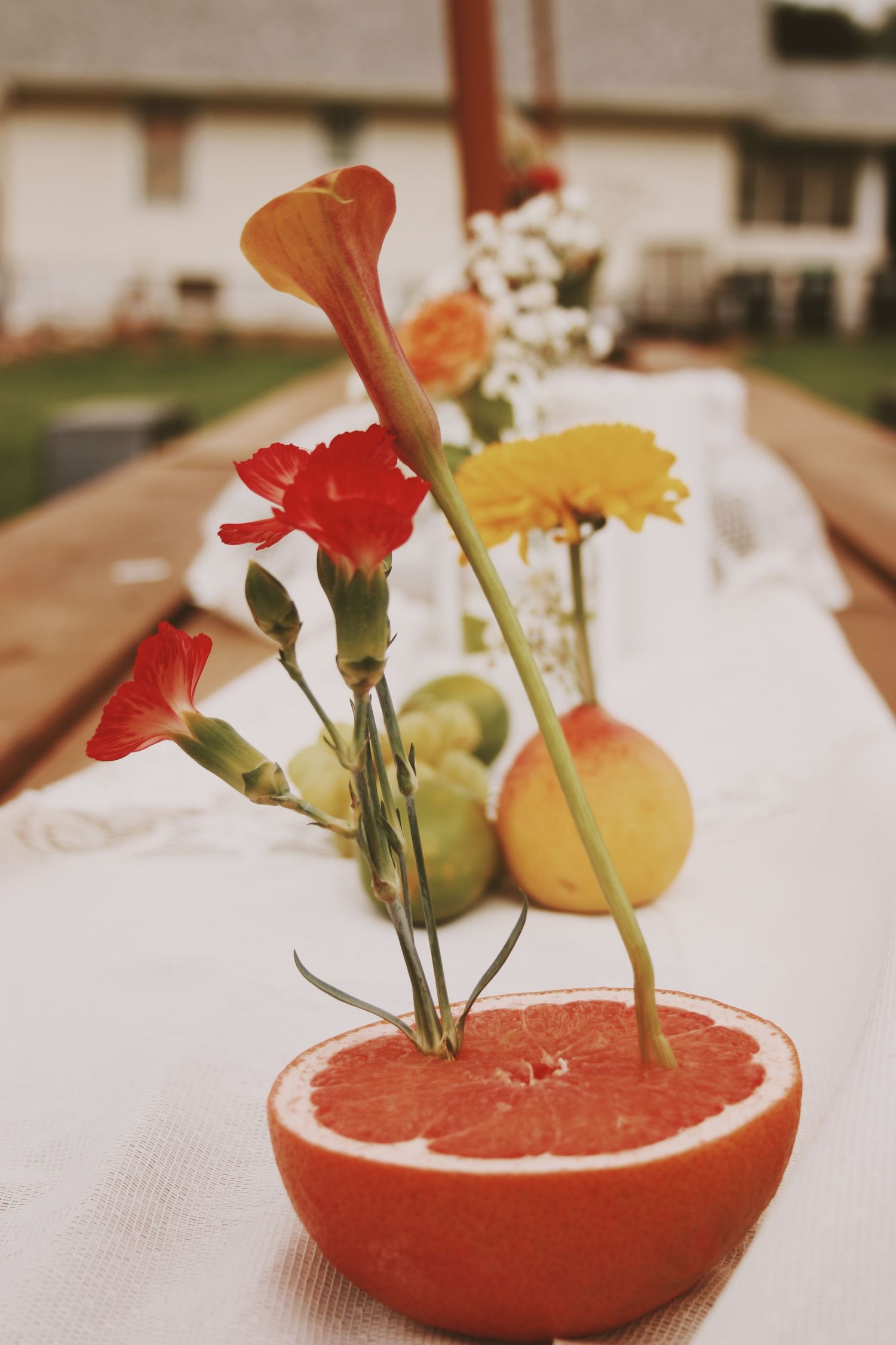 Halved grapefruit used as a vase holding colorful flowers on a white tablecloth at an outdoor garden party.