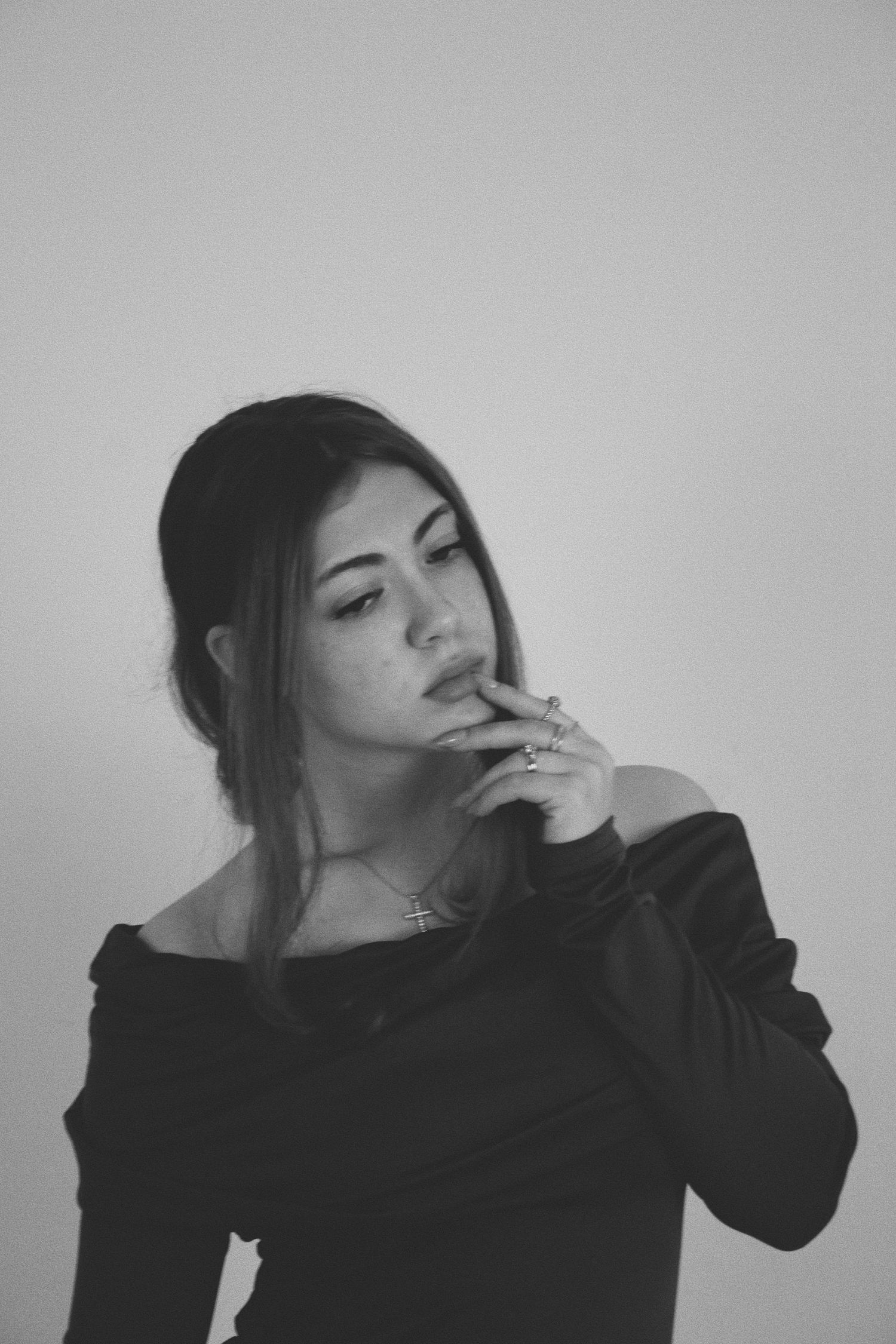 Young woman in black off-shoulder top poses thoughtfully against white background in black and white portrait.
