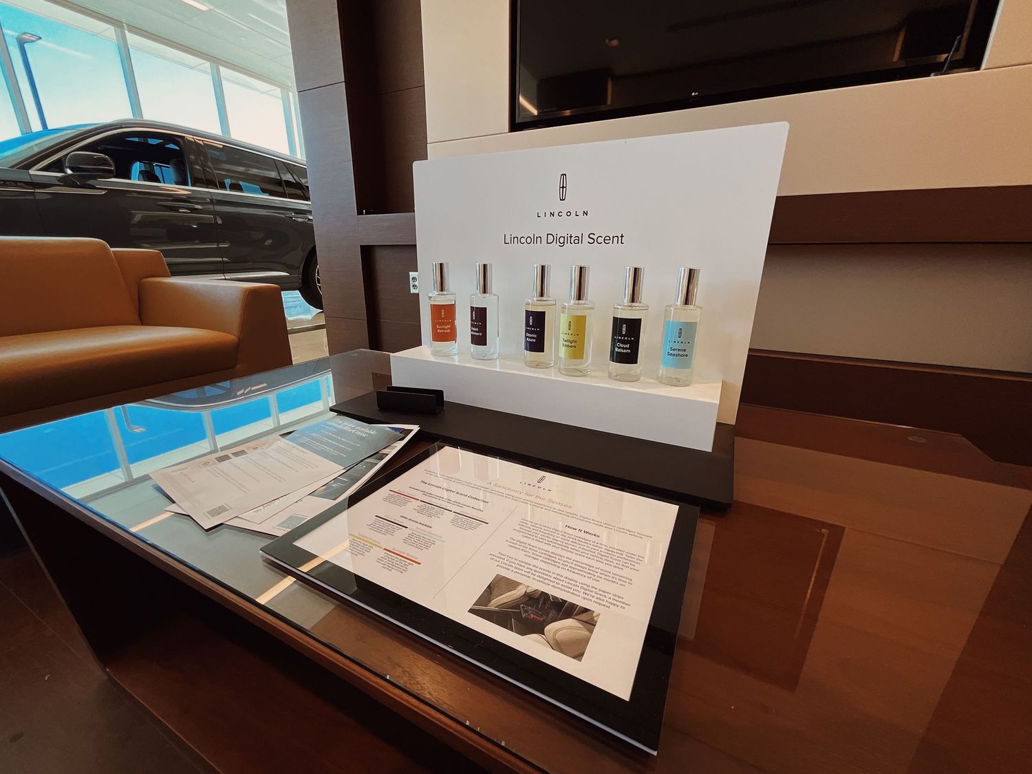 Lincoln Digital Scent display with fragrance bottles on a glass table in a modern car dealership showroom.