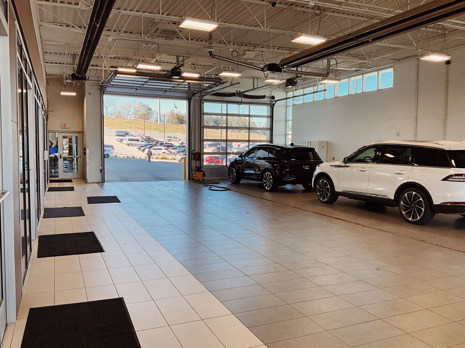 Modern car dealership service bay with black and white SUVs on lifts, featuring large garage doors and bright lighting.