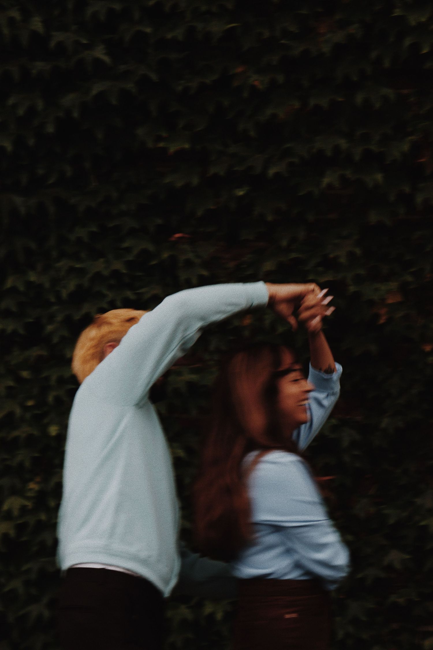A couple dancing together in front of a lush green ivy wall, captured with motion blur.