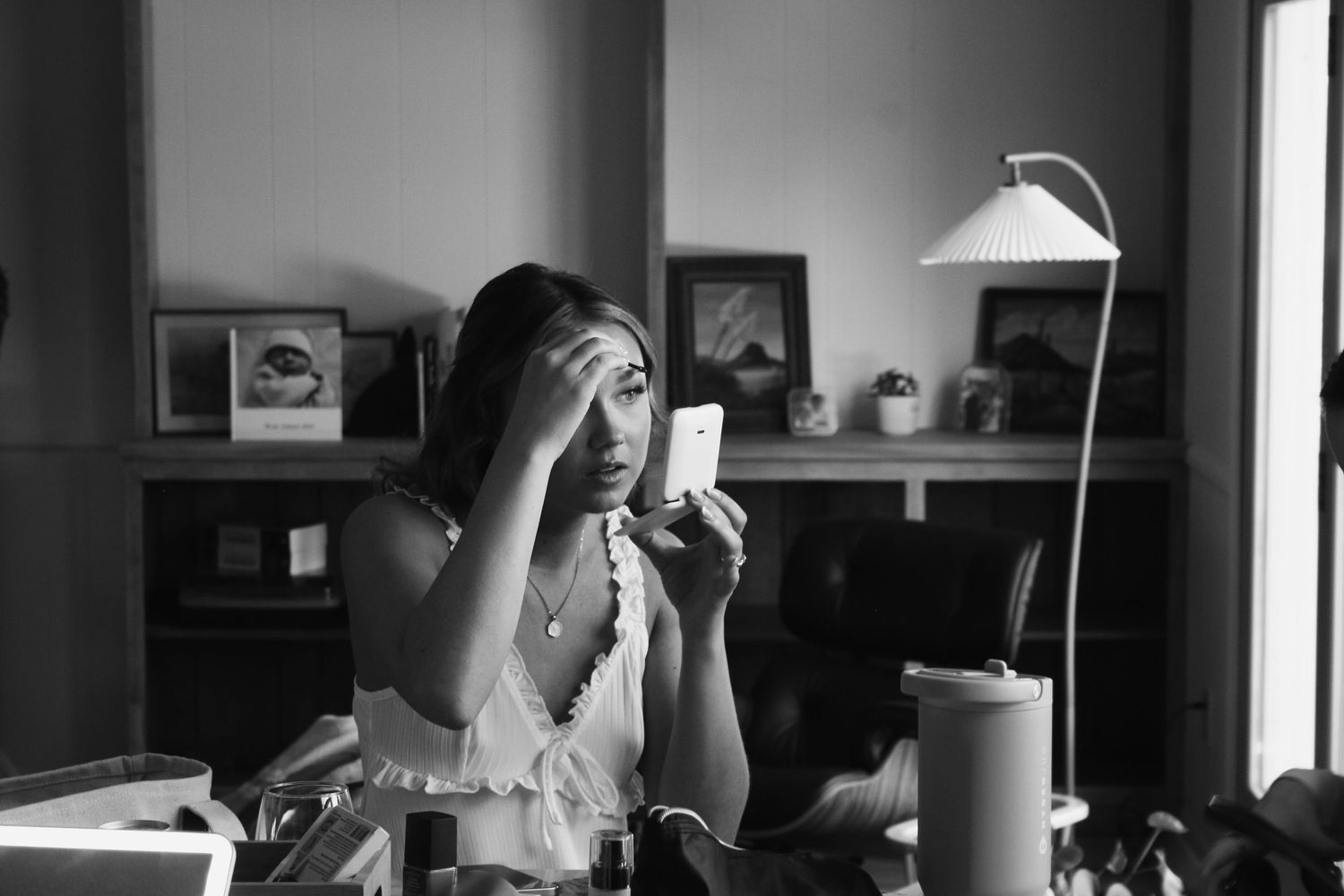 Black and white photo of a stressed woman holding a smartphone near her face while sitting at a desk indoors.