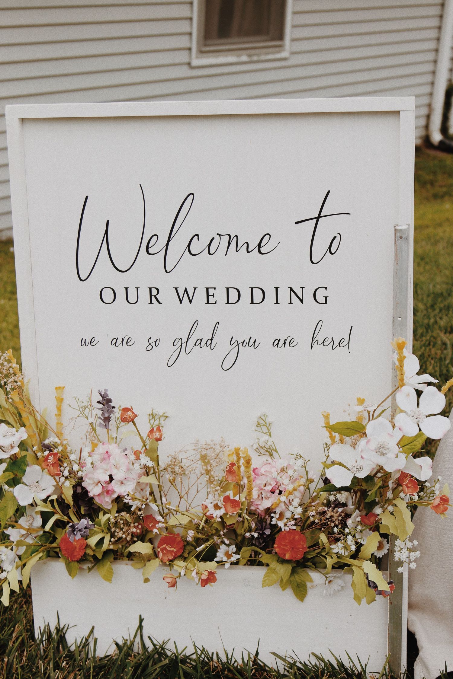 White wedding welcome sign adorned with colorful floral arrangements reading We are so glad you are here.