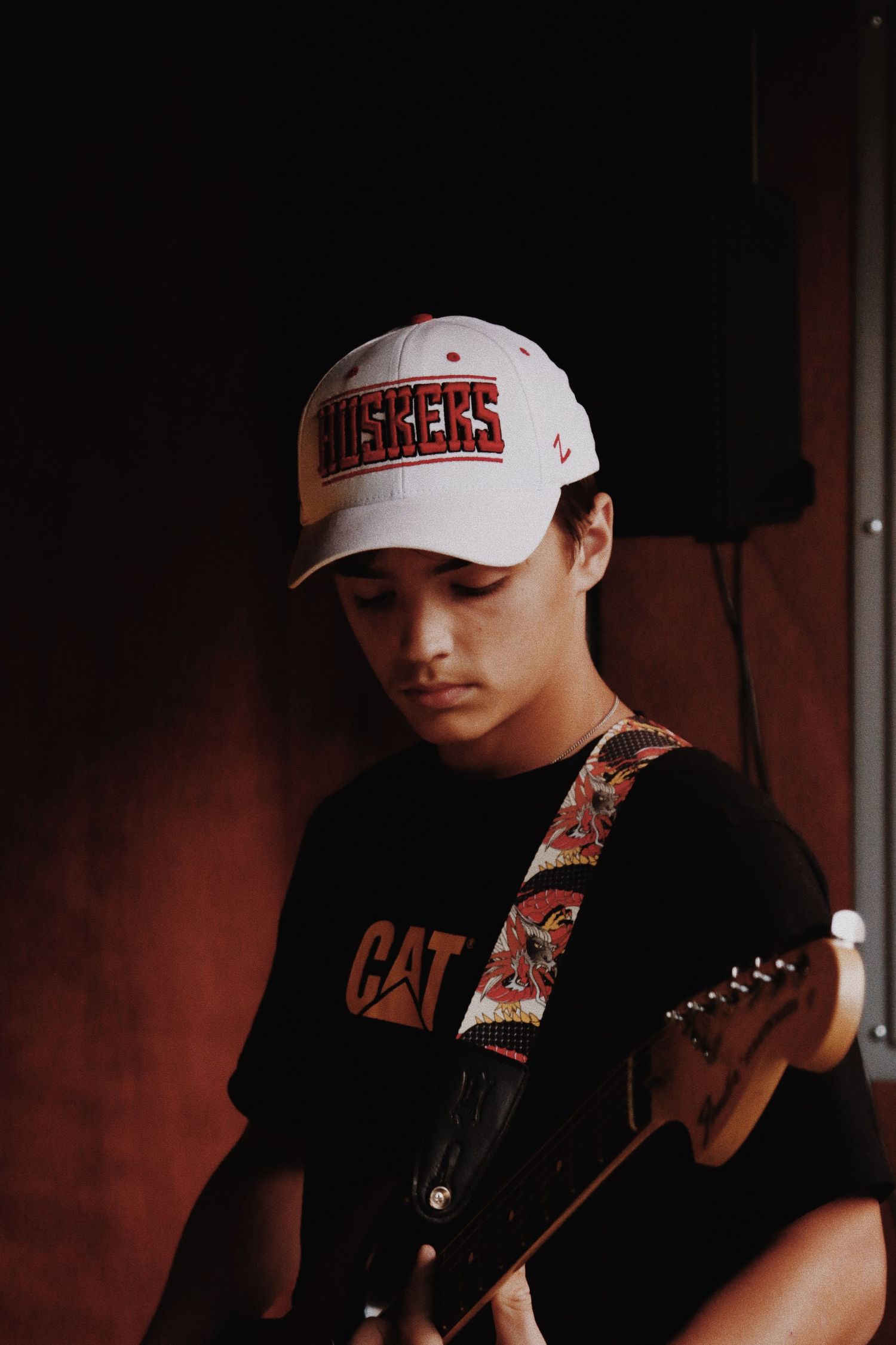 Young guitarist wearing a Huskers cap and black cat t-shirt playing electric guitar on stage.