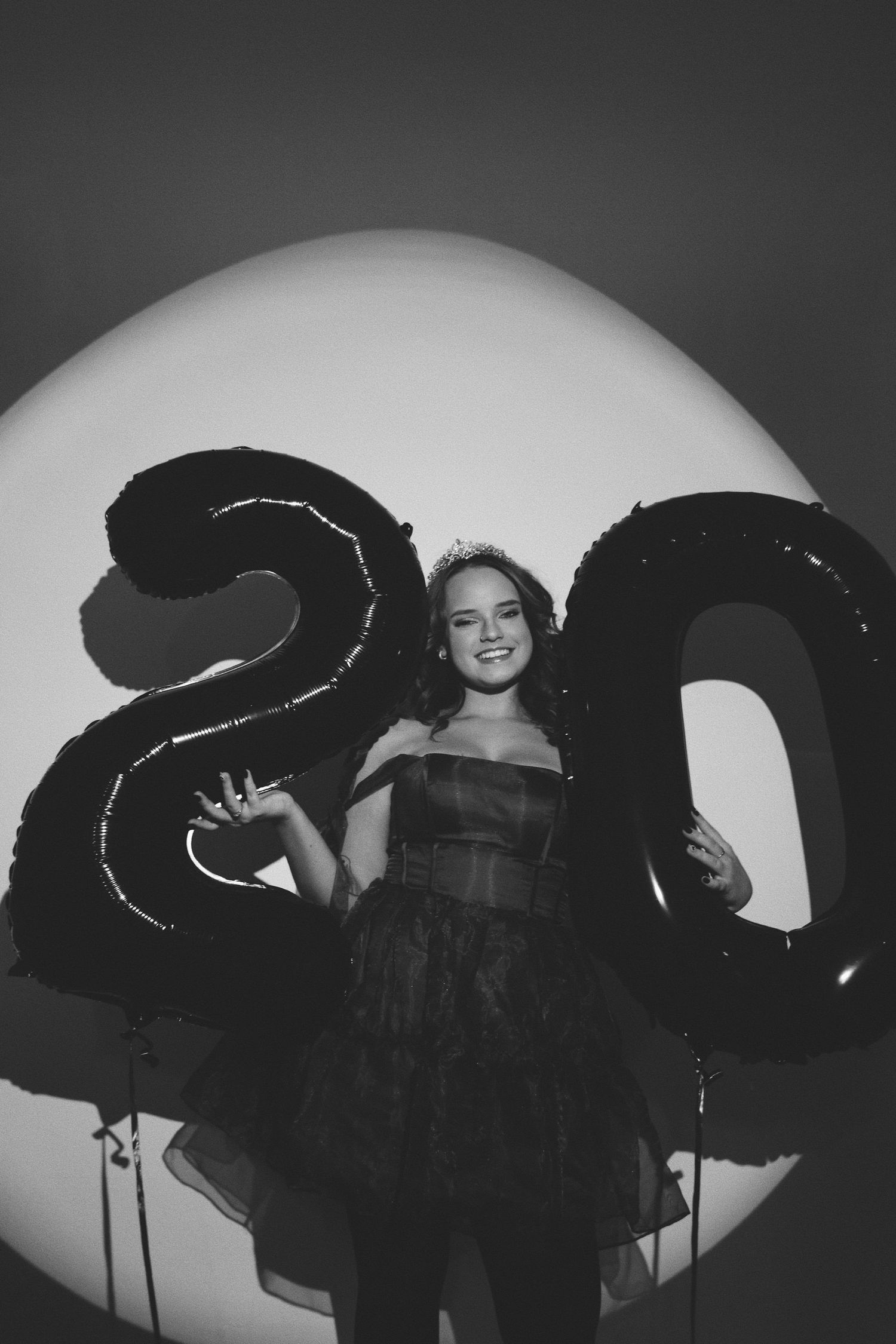 Young woman in black dress celebrating 20th birthday with large number balloons in black and white photo.