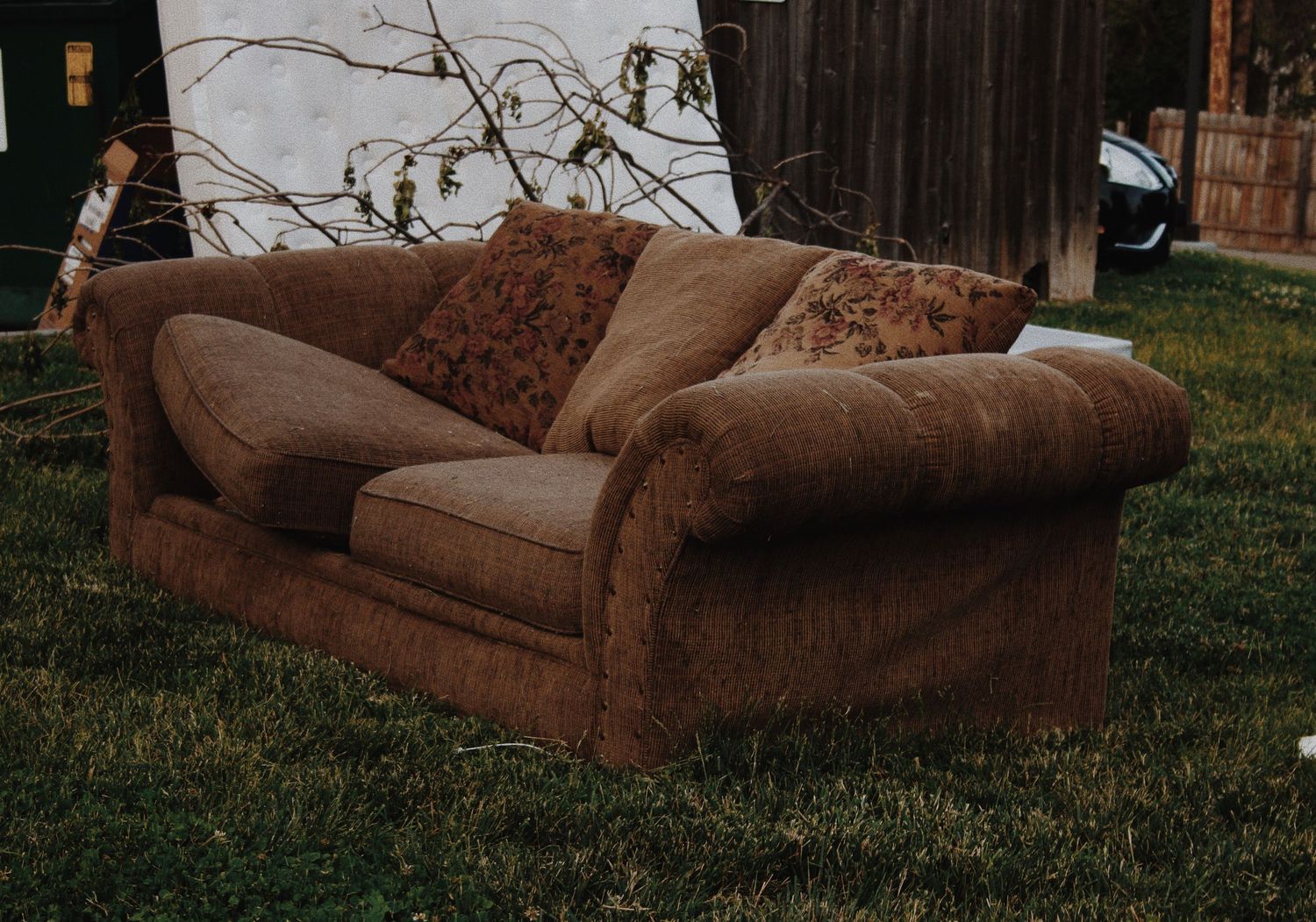 Brown microfiber loveseat sofa with decorative pillows sitting on grass in a backyard outdoor setting.