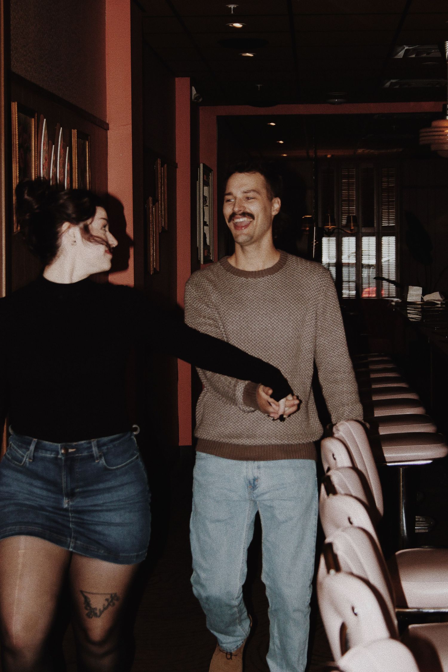 Happy couple holding hands and laughing together inside a vintage theater with pink walls.