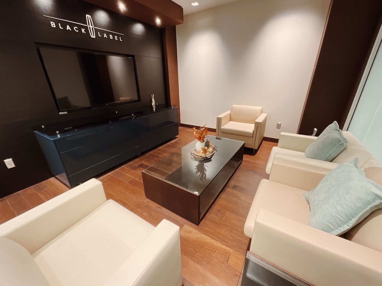 Modern Black Label luxury lounge with white sofas, glass coffee table, and wood flooring.
