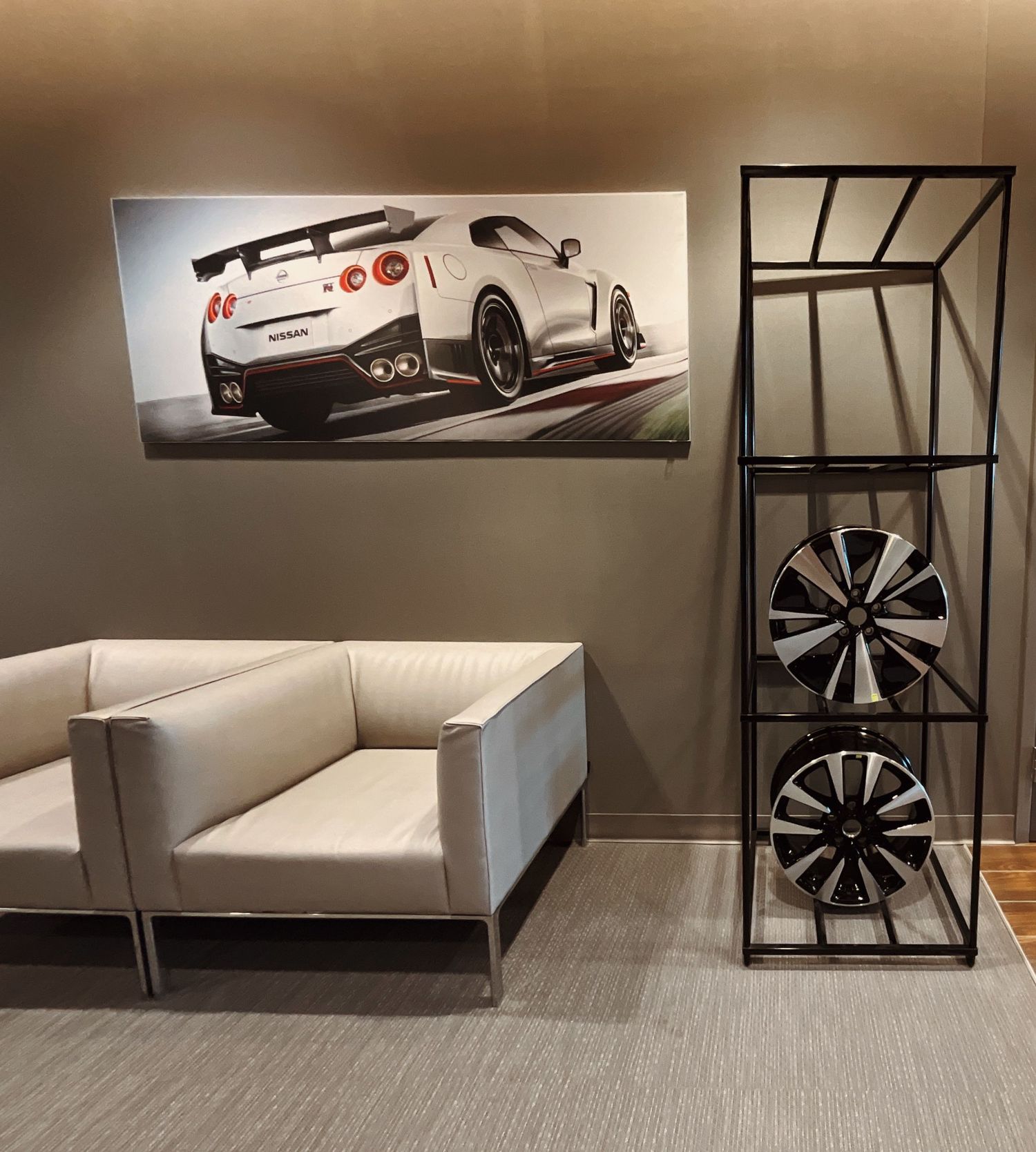 Modern car dealership lounge with white sofa, Nissan GT-R canvas art, and stylish alloy wheels display rack.