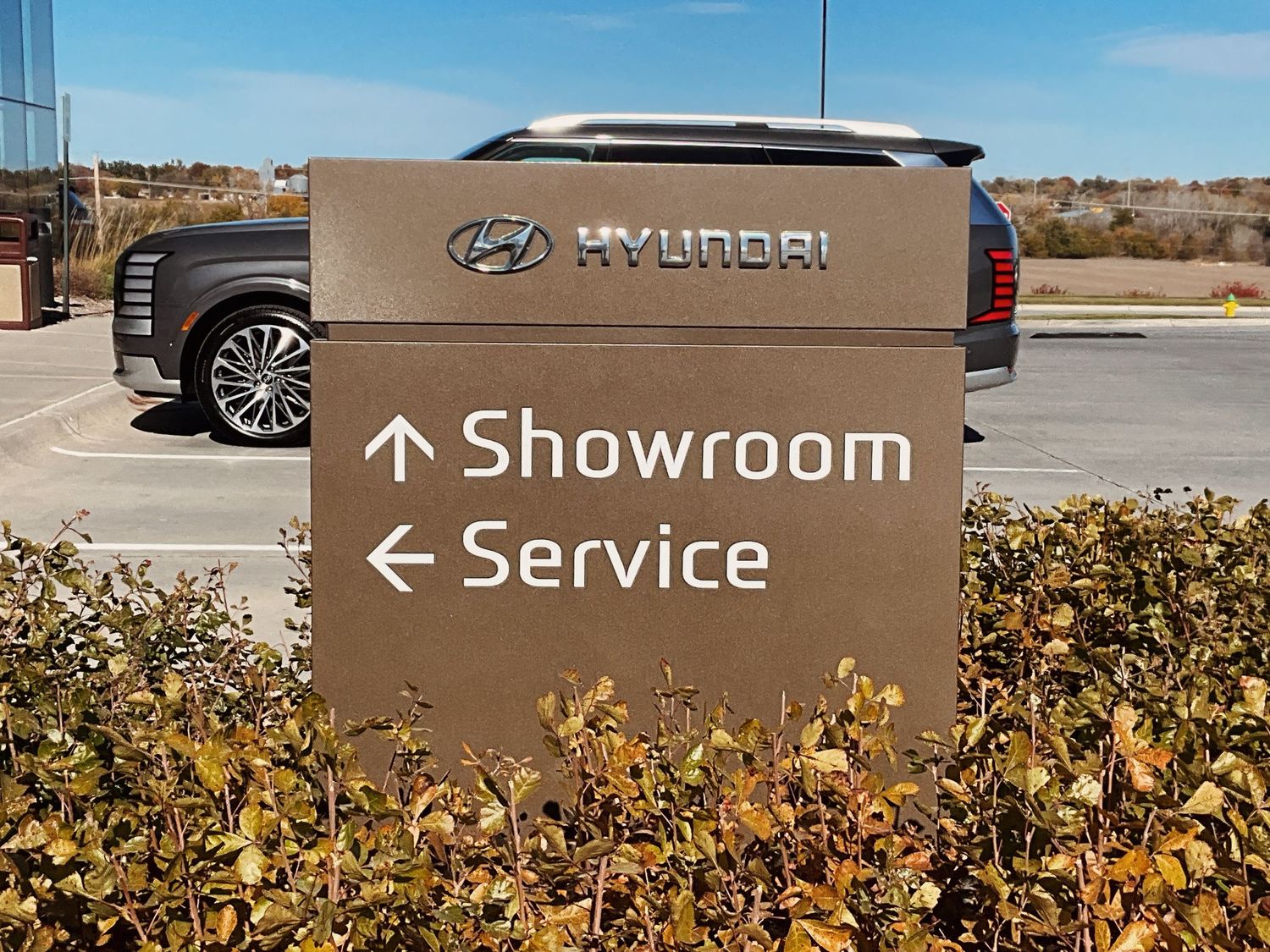 Hyundai dealership sign directing visitors to the Showroom and Service department, with an SUV parked in the background.