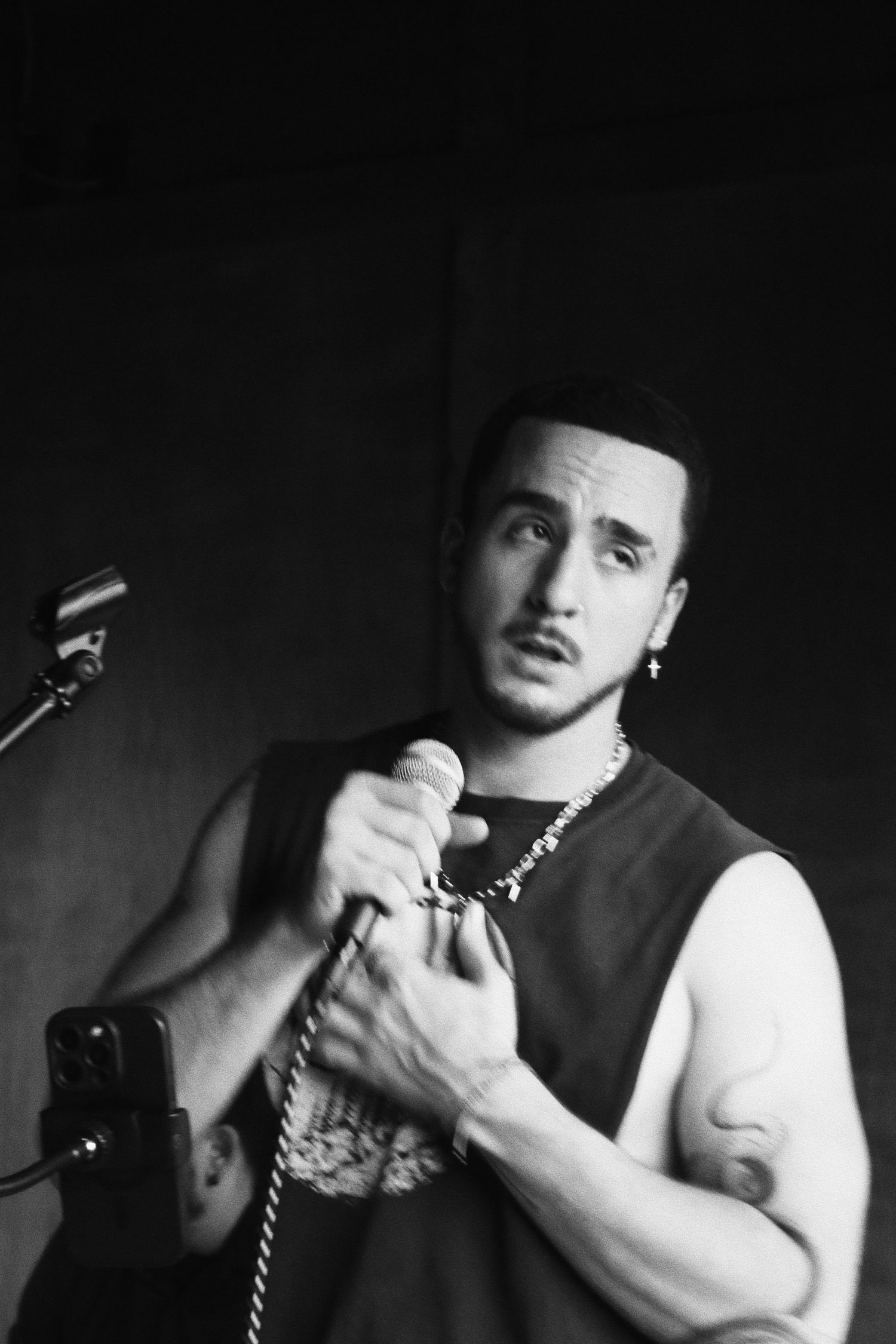 Black and white photo of a young male singer performing on stage, holding a microphone with a chain necklace.