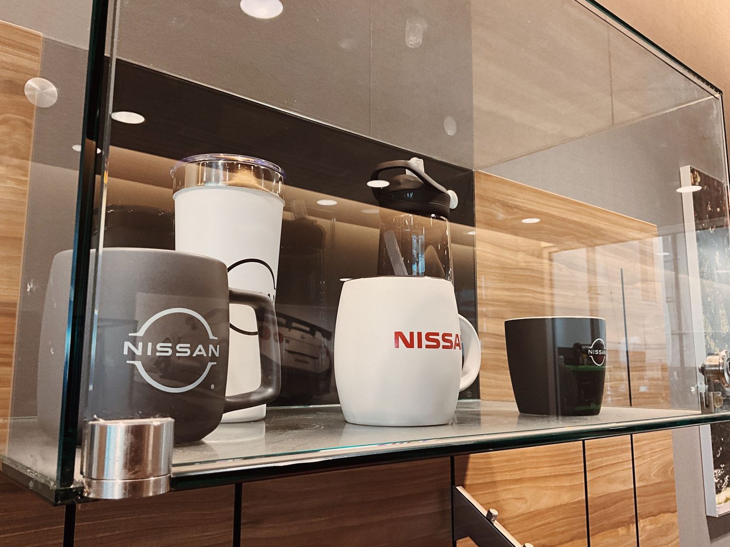Nissan branded mugs and cups displayed on a glass shelf in a modern showroom setting.