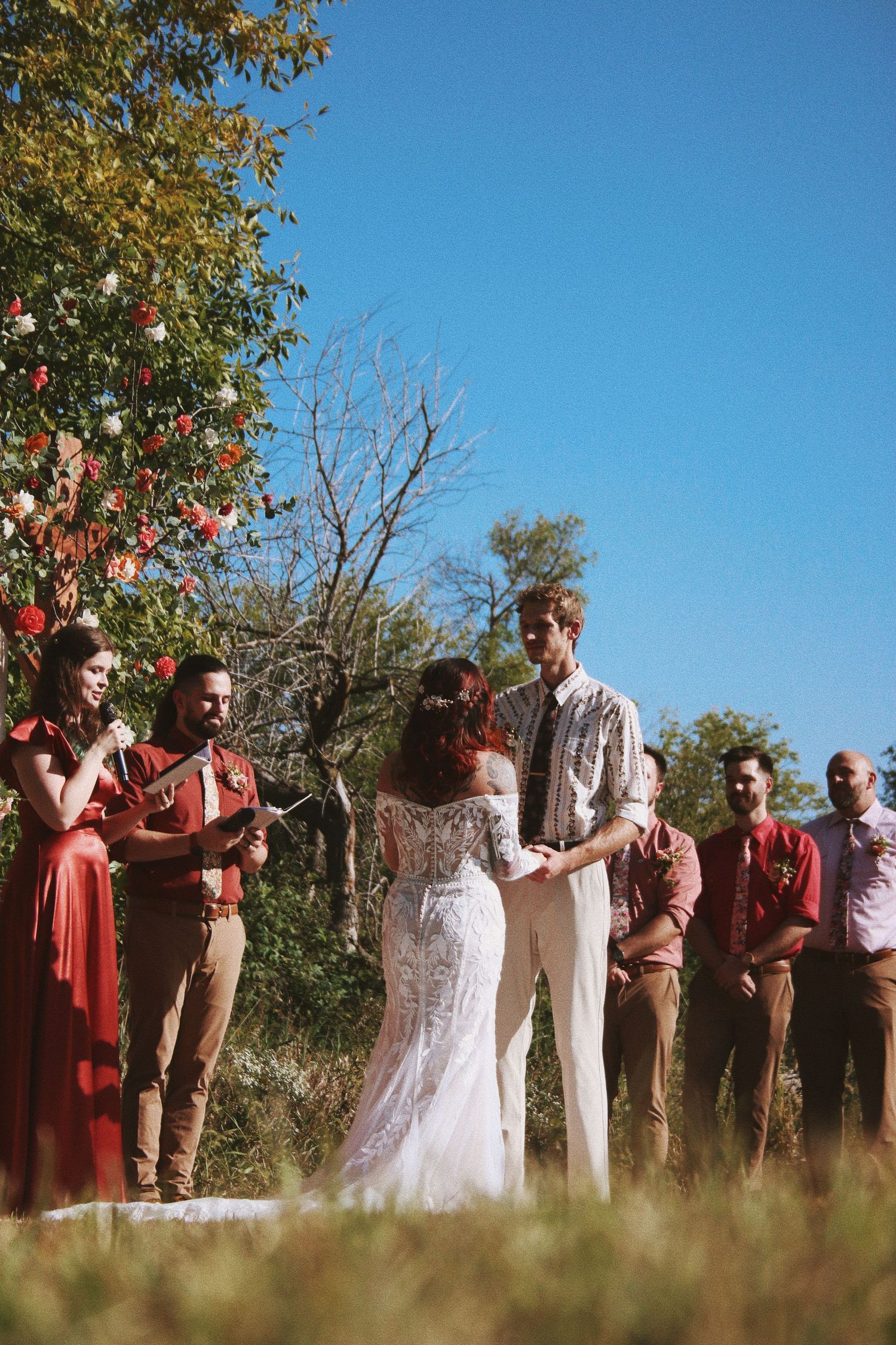 Outdoor boho wedding ceremony with bride and groom exchanging vows under blue sky.