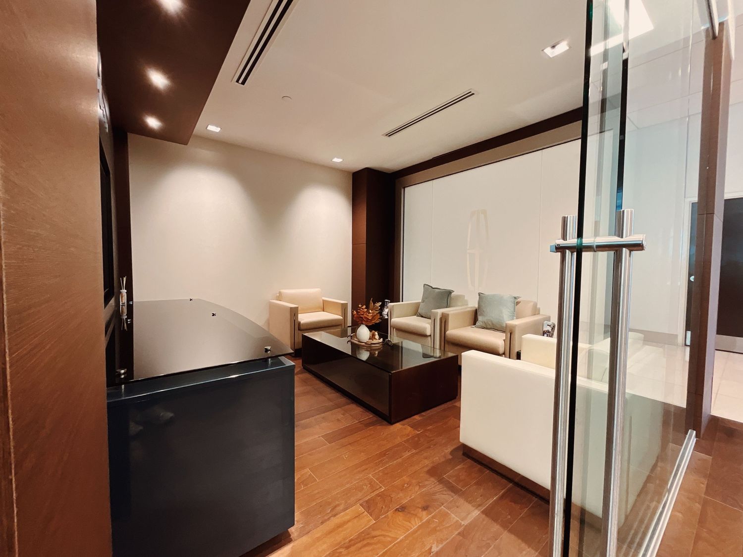Modern office lounge with white sofas, glass partition walls, and polished hardwood floors in a contemporary corporate setting.