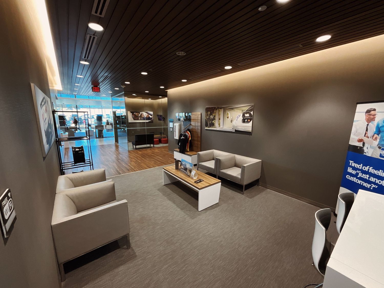 Modern retail store waiting area with gray sofas, wood coffee table, and sleek dark ceiling with ambient lighting.