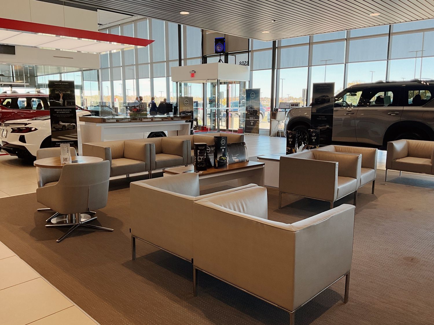 Modern car dealership showroom featuring a comfortable lounge area with beige sofas and chairs near large windows.