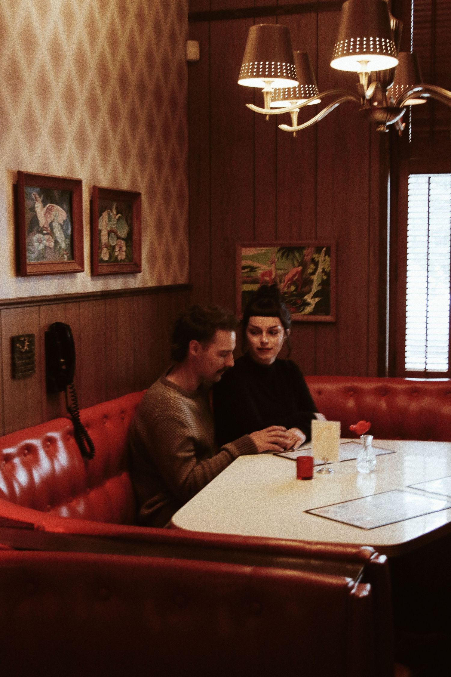 Couple sitting together in a cozy retro diner booth with red leather seats, warm lighting, and vintage wall art.