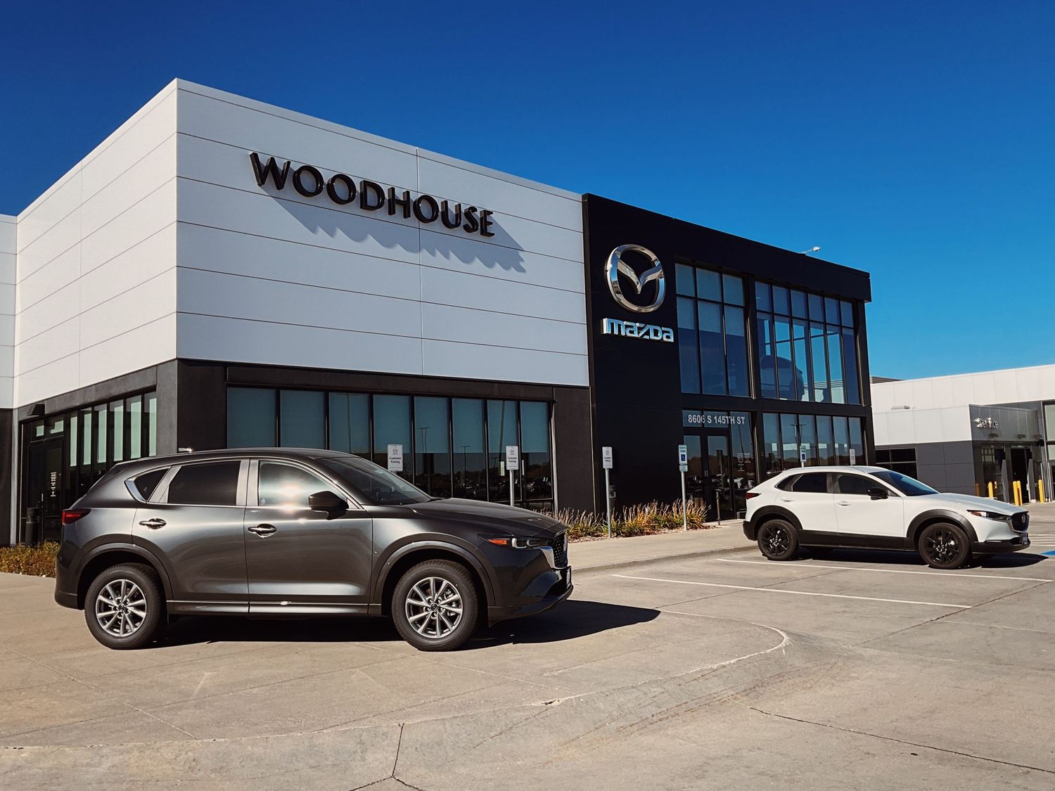 Woodhouse Mazda dealership exterior with two SUVs parked in front of a modern building.