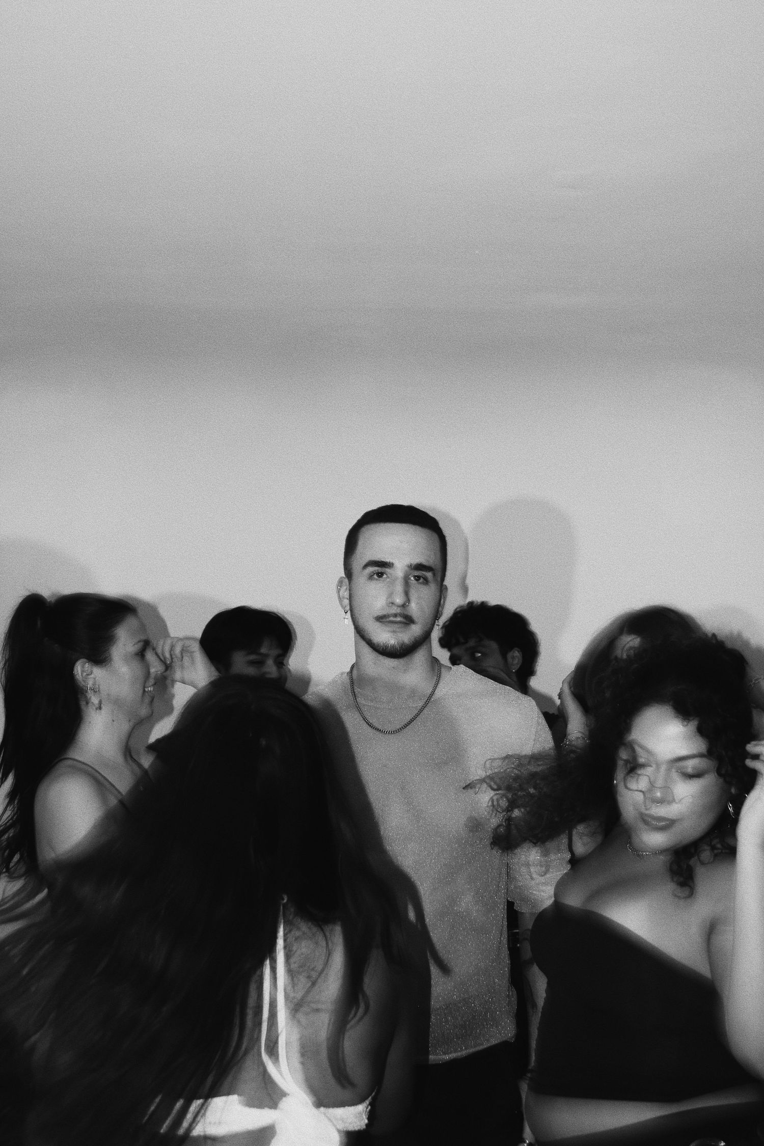 Black and white photo of a young man standing among a crowd of people at a social gathering or party.