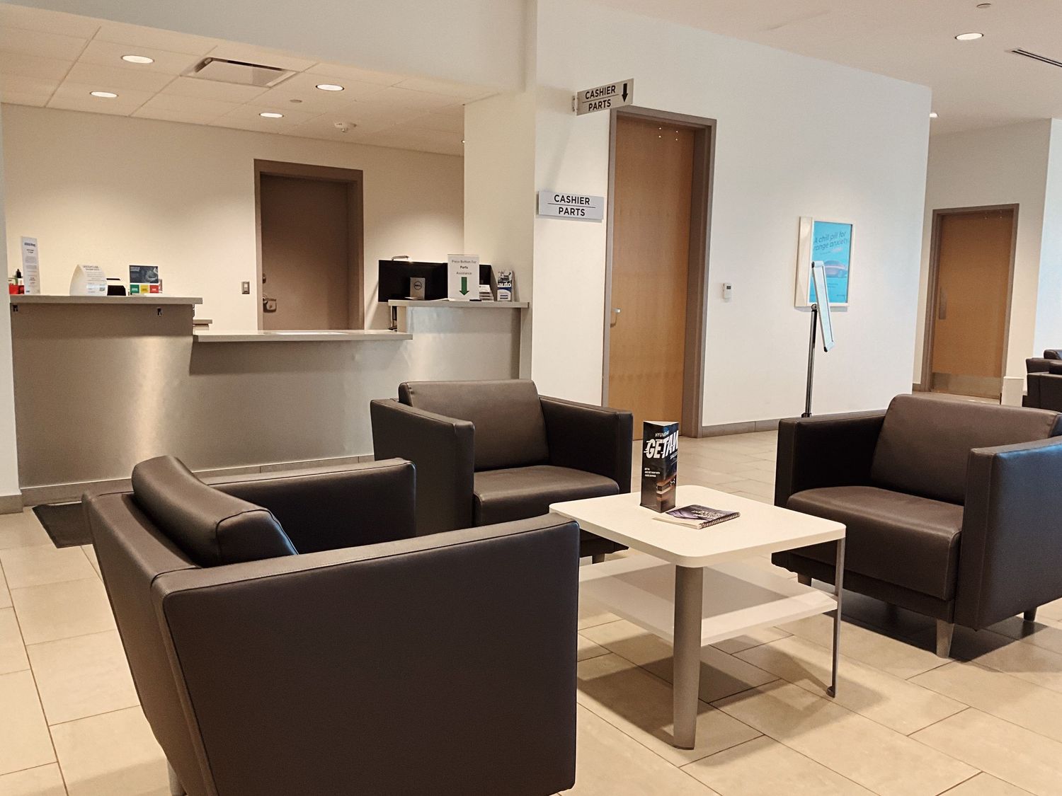 Modern medical office waiting room with dark leather chairs, coffee table, reception desk, and wood accent doors.