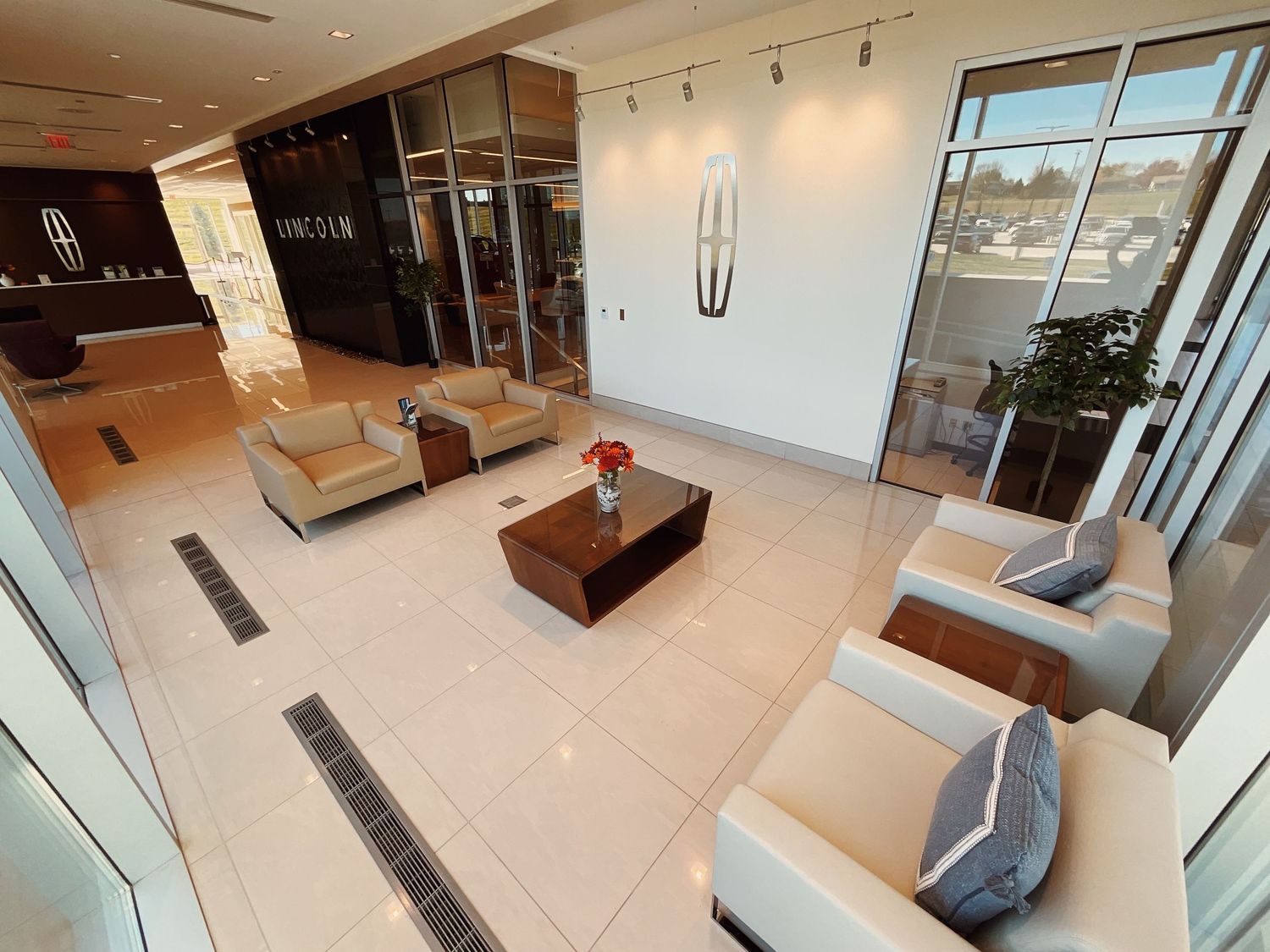 Elegant Lincoln dealership showroom with beige leather seating, marble floors, and modern decor viewed from above.