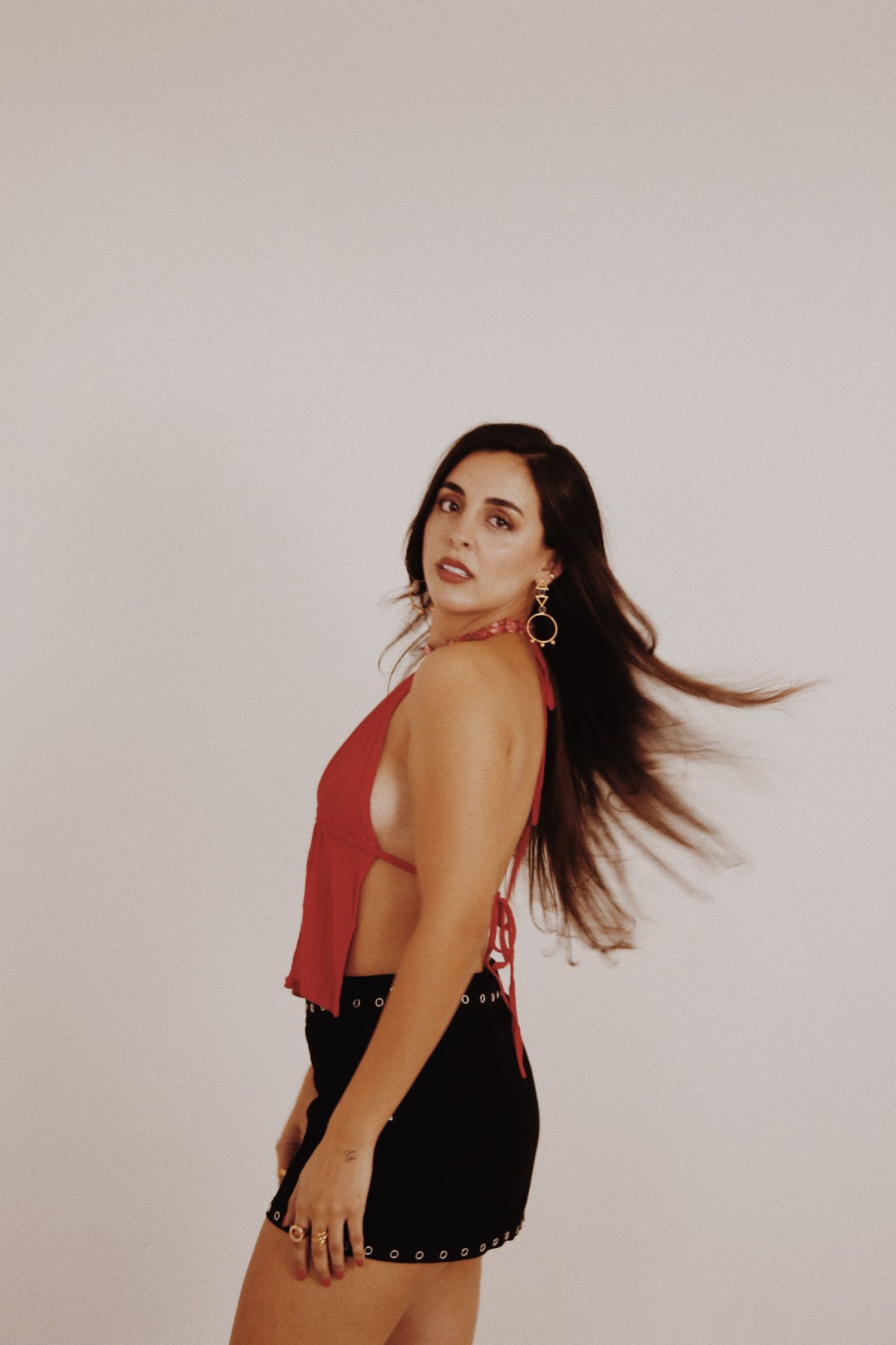 Young woman in red halter top and black mini skirt posing dynamically with hair flowing against white background.