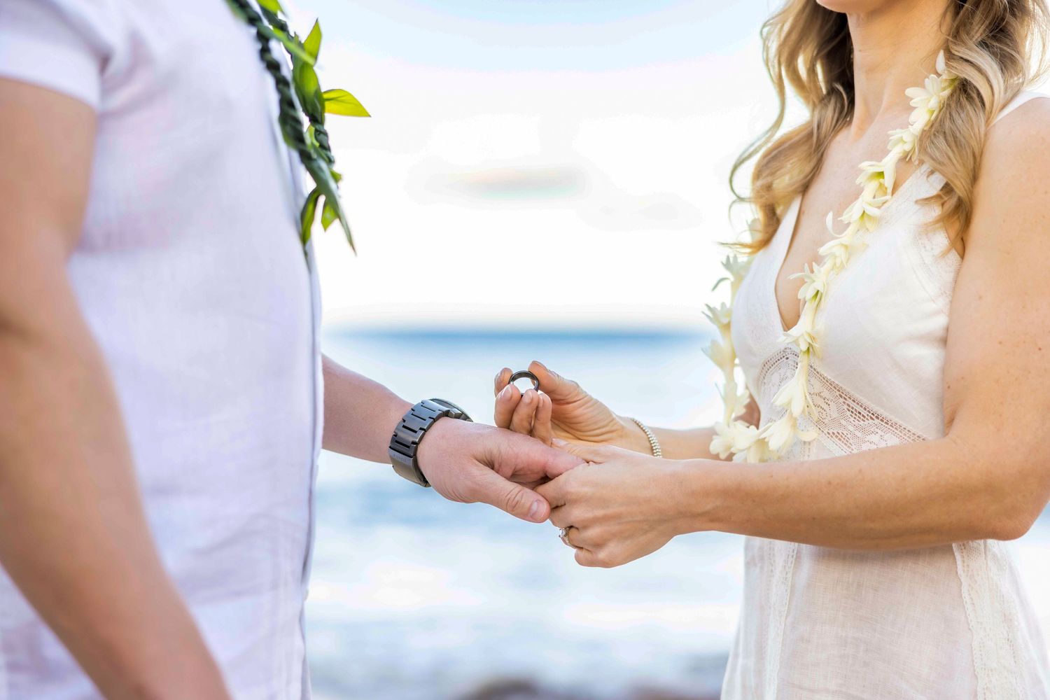 Couple exchanging rings in a beachside ceremony, wearing leis with the ocean in the background. Wailea