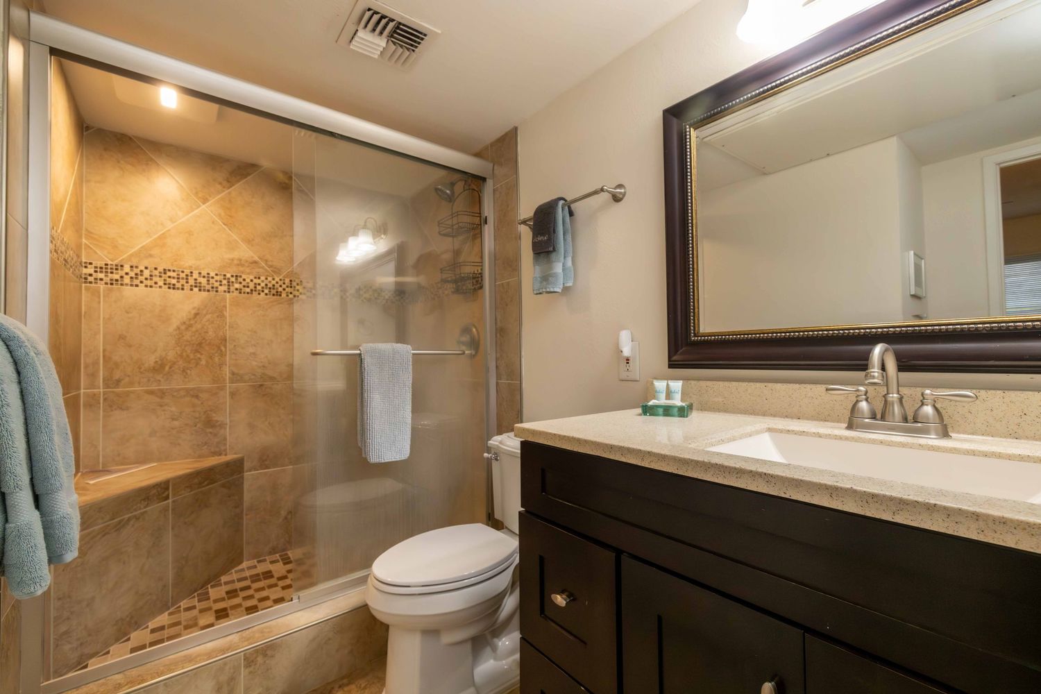 Modern bathroom with a tiled walk-in glass shower, dark wood vanity, granite countertop, framed mirror, and white toilet.