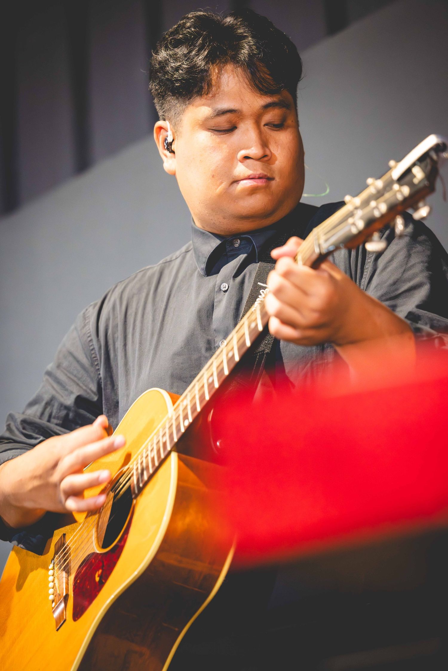 Musician in a dark button-up shirt with eyes closed plays a yellow acoustic guitar during a live performance.
