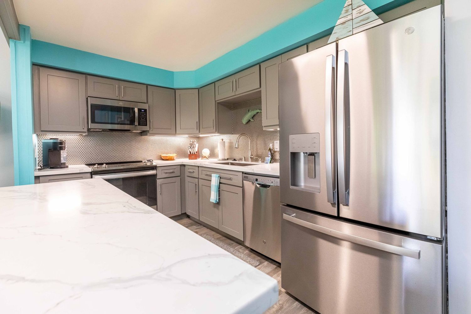 Modern kitchen with gray cabinets, stainless steel appliances, white marble-look quartz countertop, and teal accent walls.