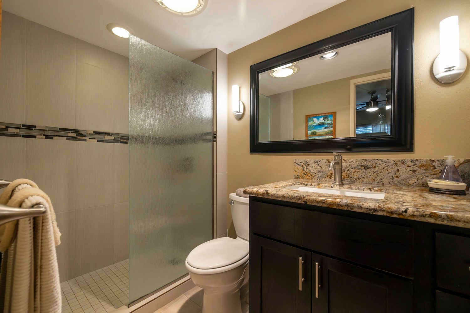 Modern bathroom with a frosted glass walk-in shower, granite countertop vanity, dark wood cabinets, framed mirror, and a white toilet.