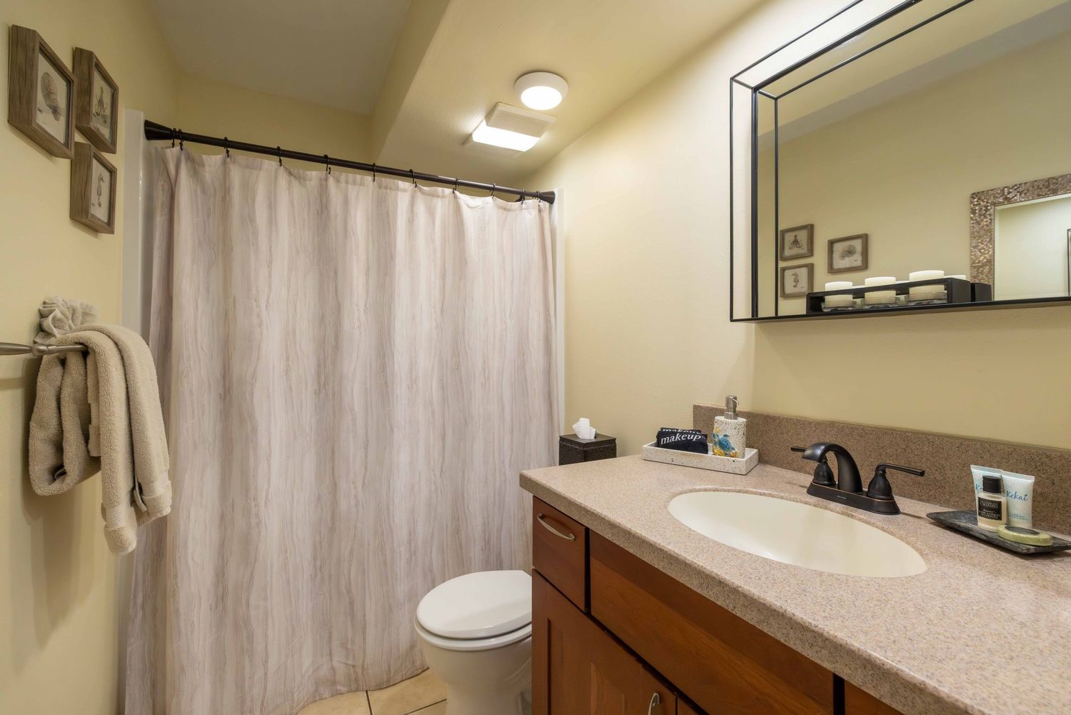 Cozy bathroom with a granite-top wood vanity, large framed mirror, toilet, and a striped shower curtain beside a hanging towel and wall art.