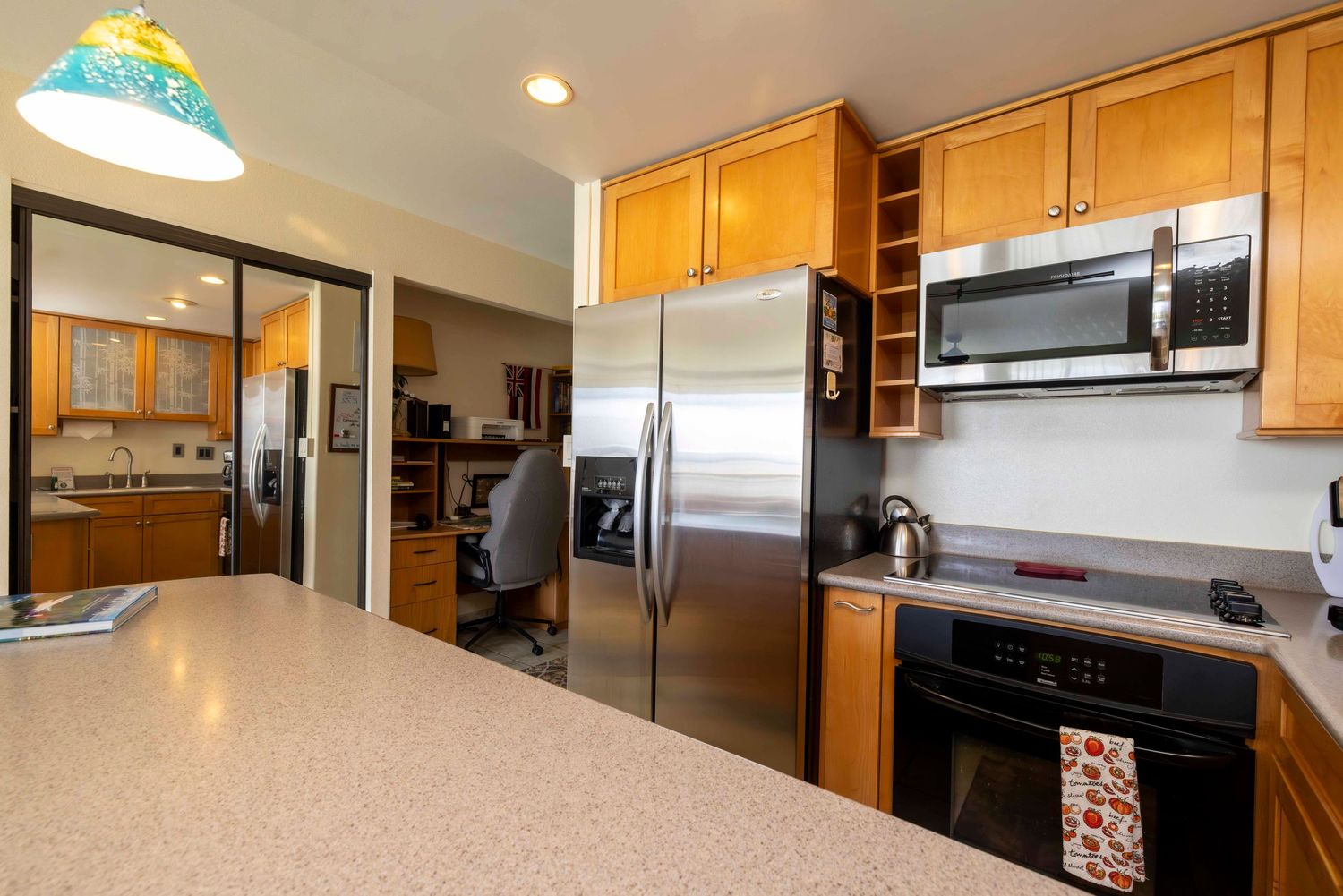 Bright kitchen with stainless steel refrigerator, built-in microwave, black oven, light wood cabinets, and a granite countertop.